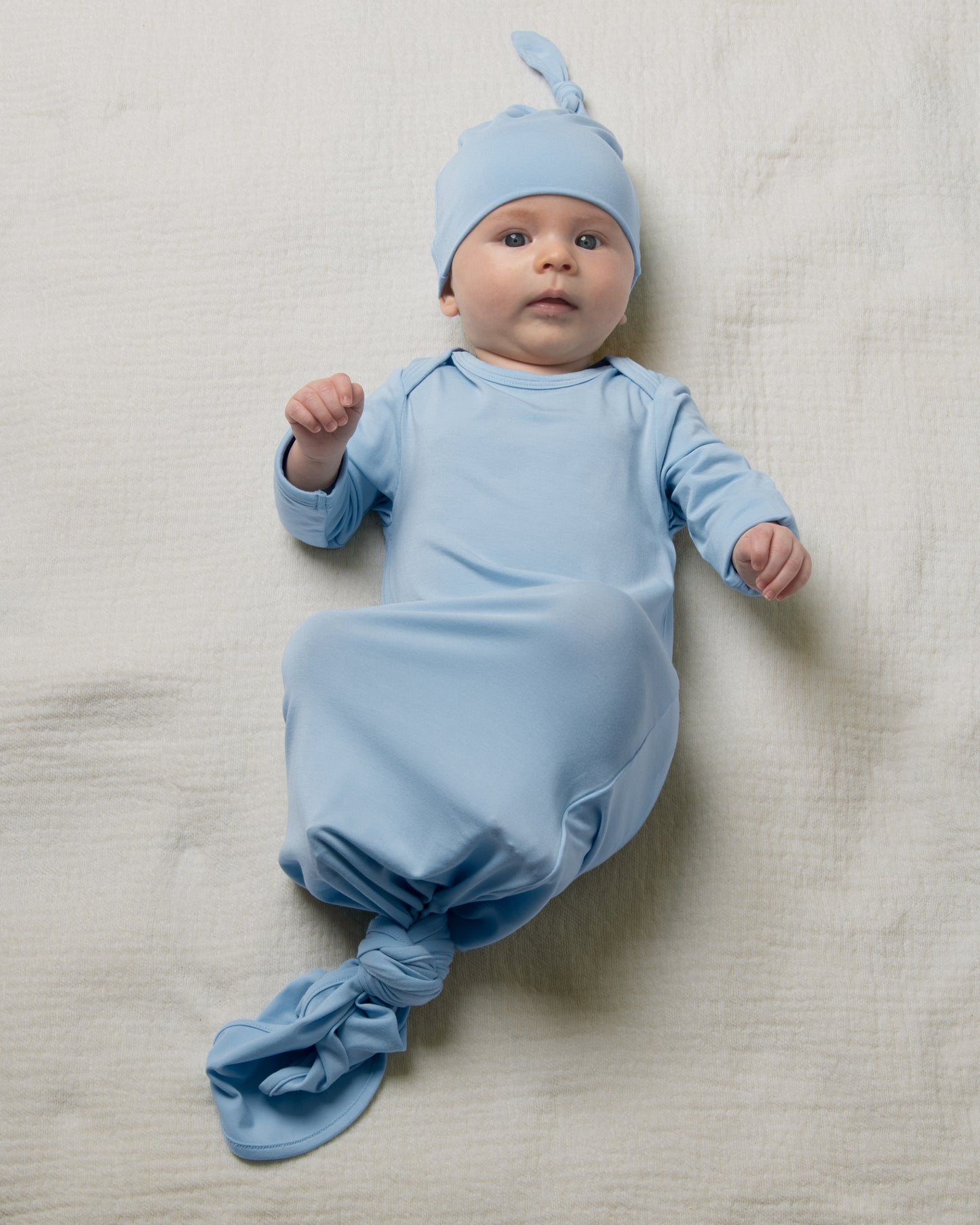 Baby in Bamboo Knotted Baby Gown in French Blue lying on a light-colored blanket@model_info:Danny is 3 months old.