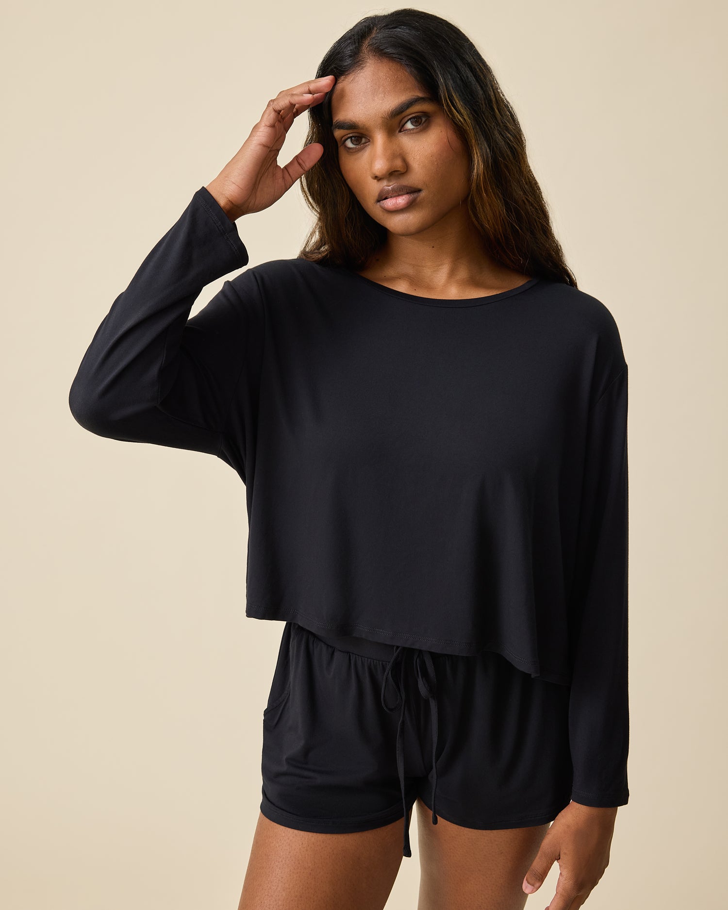 Woman wearing the Aria Bamboo Casual Cropped Long Sleeve Top in black with matching shorts on a beige background