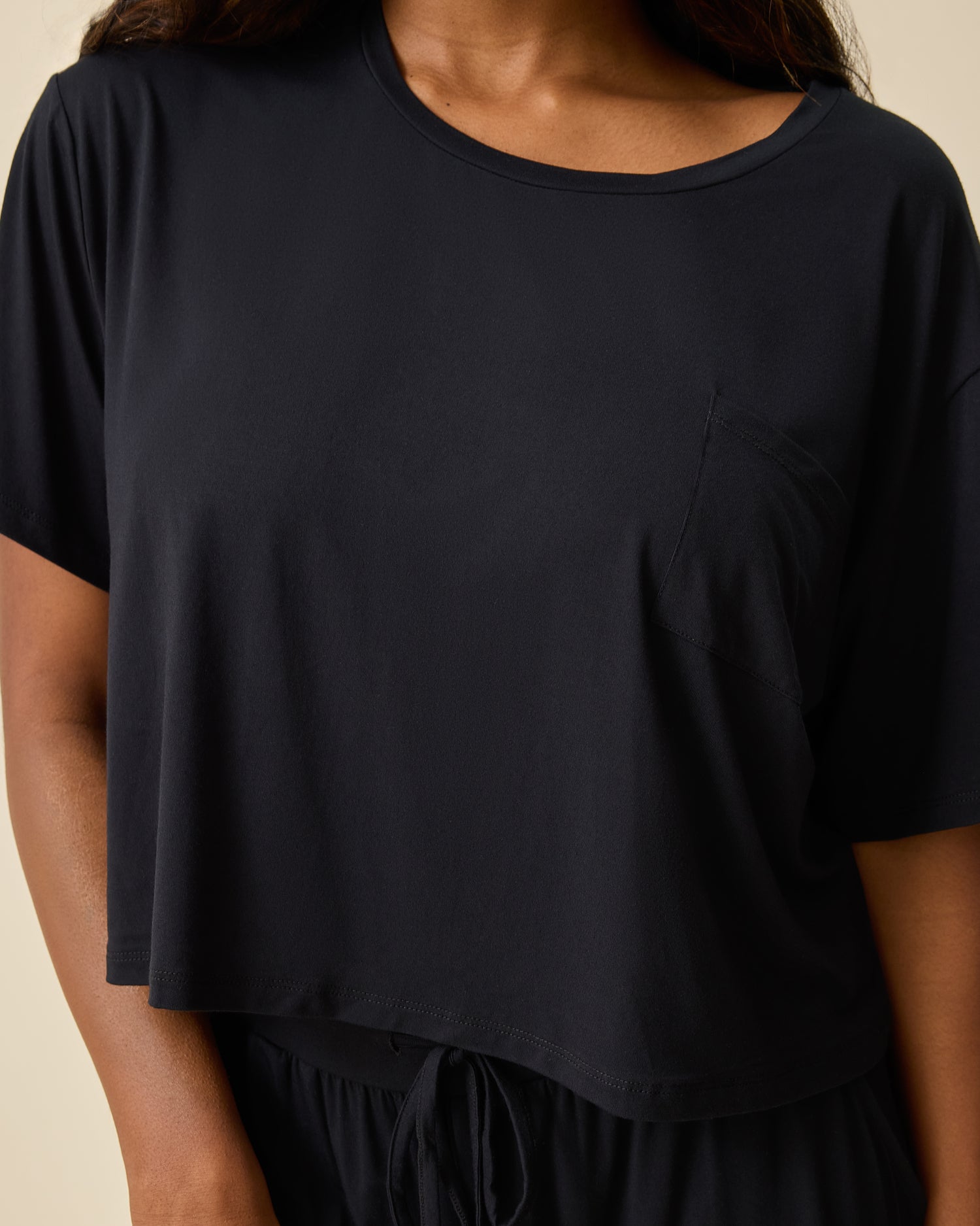 Close up of woman wearing the Aria Bamboo Casual Cropped Short Sleeve Top in black on beige background