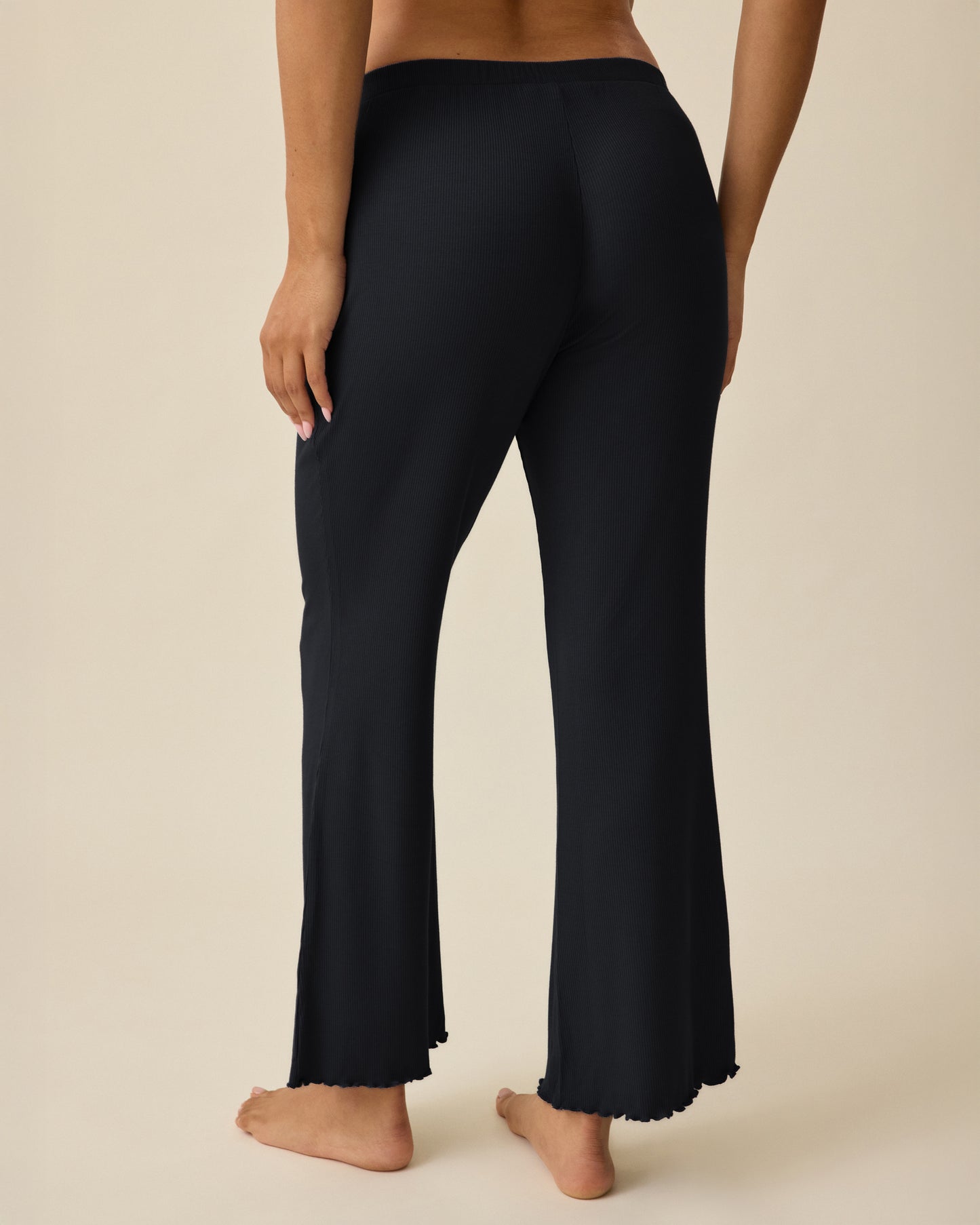 Model is wearing Ribbed Modal Lounge Pant in Black on a beige background. 