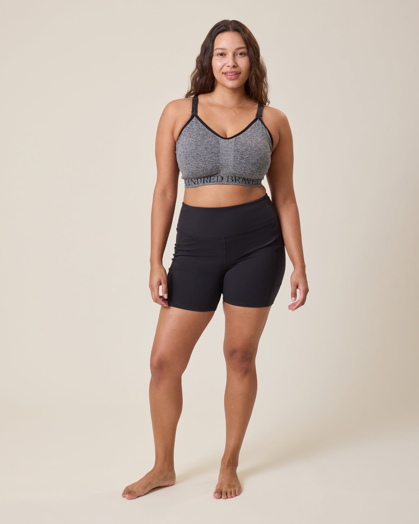 Woman wearing a gray sports bra with the Stevie Active Postpartum Bike Short in black on a beige background