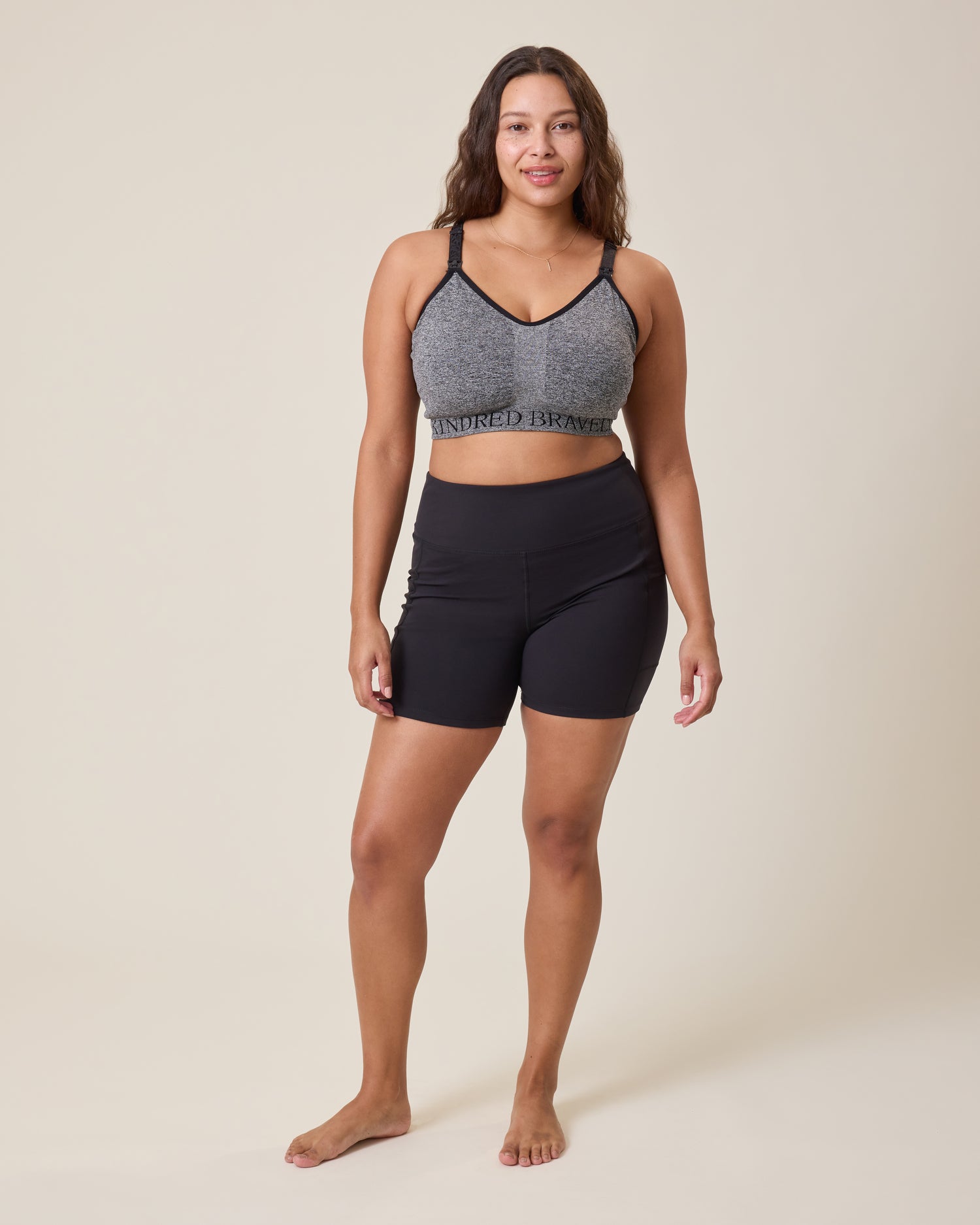 Woman wearing a gray sports bra with the Stevie Active Postpartum Bike Short in black on a beige background