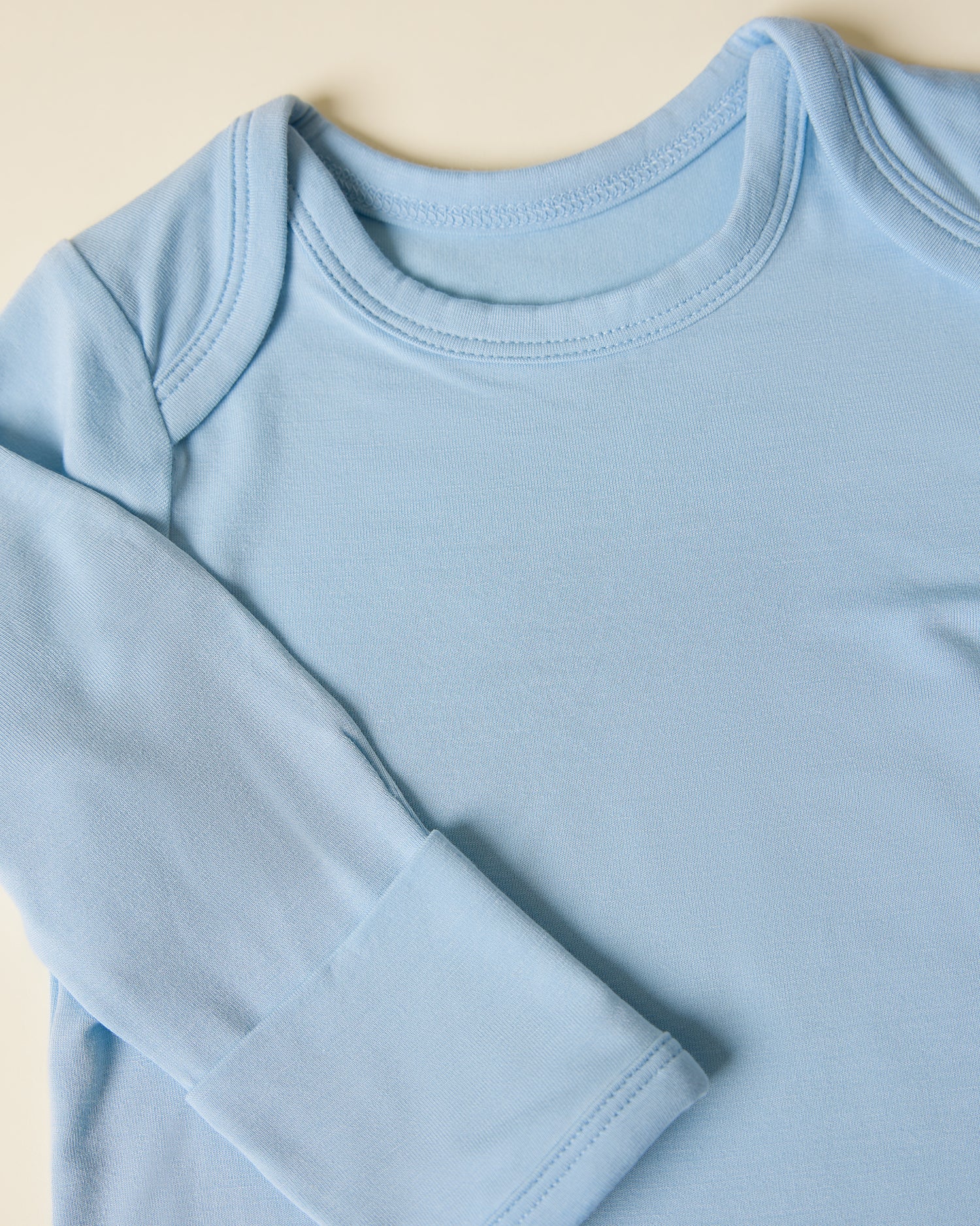 Close-up of Bamboo Knotted Baby Gown & Hat in light french blue on a beige background