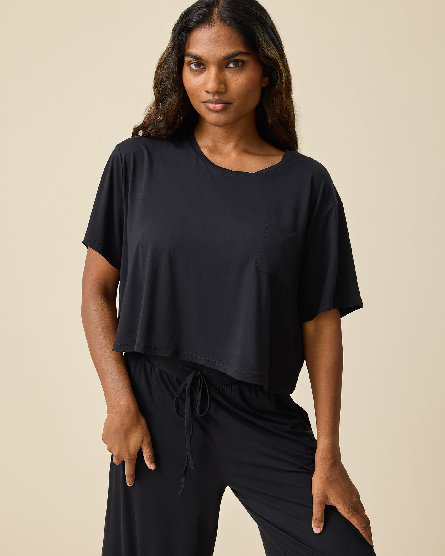 Woman wearing the Aria Bamboo Casual Cropped Short Sleeve Top in black with matching pants on a beige background