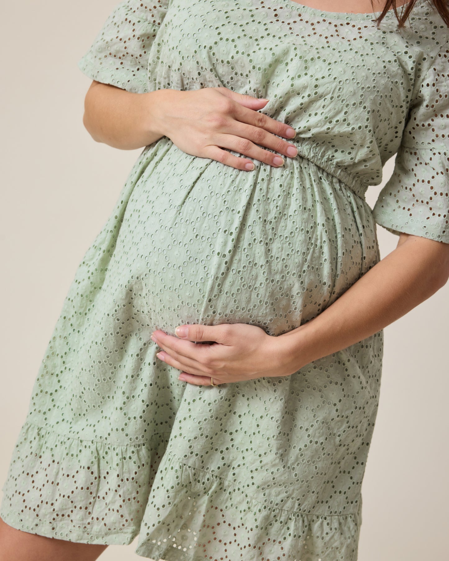 Pregnant person wearing the Dahlia Eyelet Maternity & Nursing Dress in aqua mist on a beige background