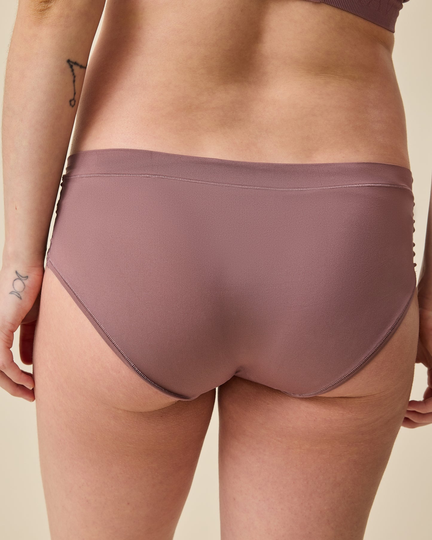Back view of model wearing Grow with Me™ Maternity & Postpartum Hipster in Twilight on a beige background