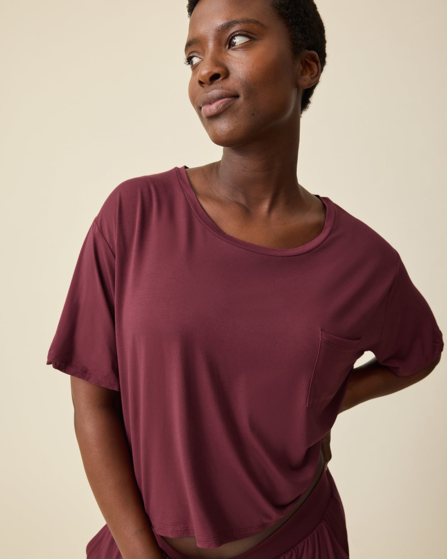 Model is wearing Aria Bamboo Casual Cropped Short Sleeve Top in Deep Burgundy and Aria Bamboo Casual Lounge Short in Deep Burgundy, on a beige background. 