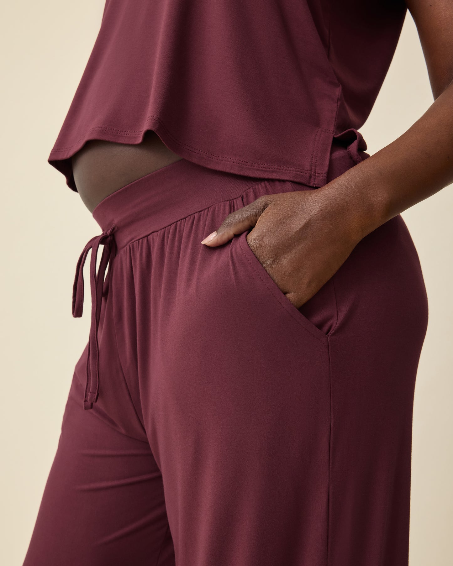 Side view of Aria Bamboo Cropped V-neck Tank in Deep Burgundy and Aria Bamboo Casual Lounge Pant in Deep Burgundy on a beige background.