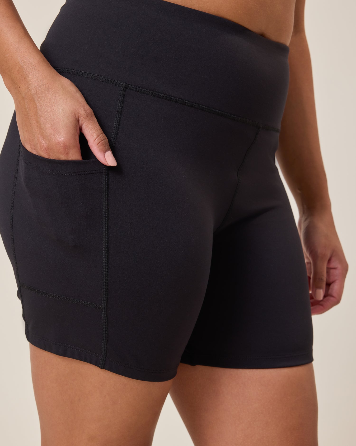 Stevie Active Postpartum Bike Short in black worn by a person with hand in pocket on a neutral background