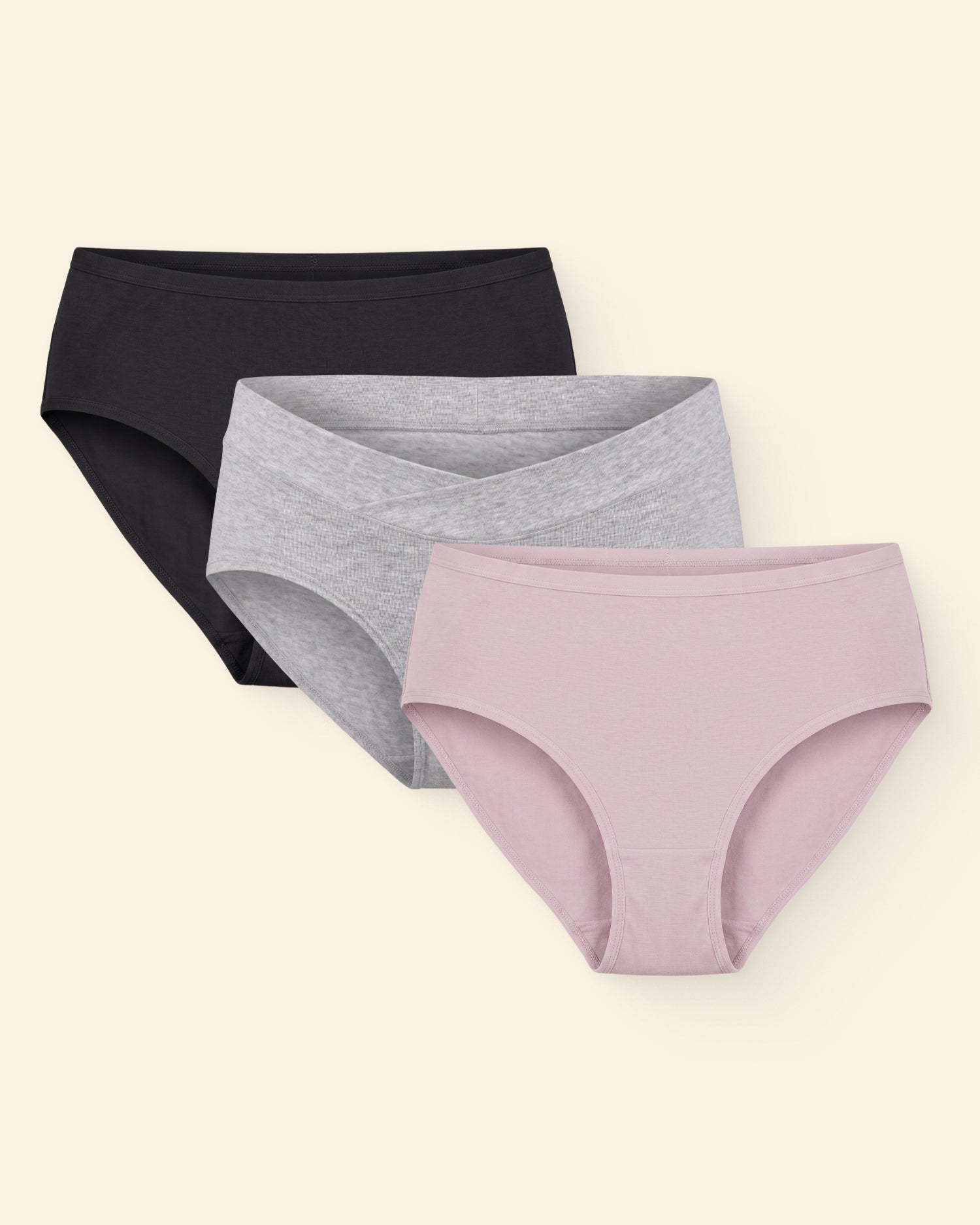 Flat lays of SoftStretch Cotton Maternity & Postpartum Hipster in Black, Bamboo Maternity & Postpartum Hipster in Grey Heather, and SoftStretch Cotton Maternity & Postpartum Hipster in Lilac Mist on a beige background.