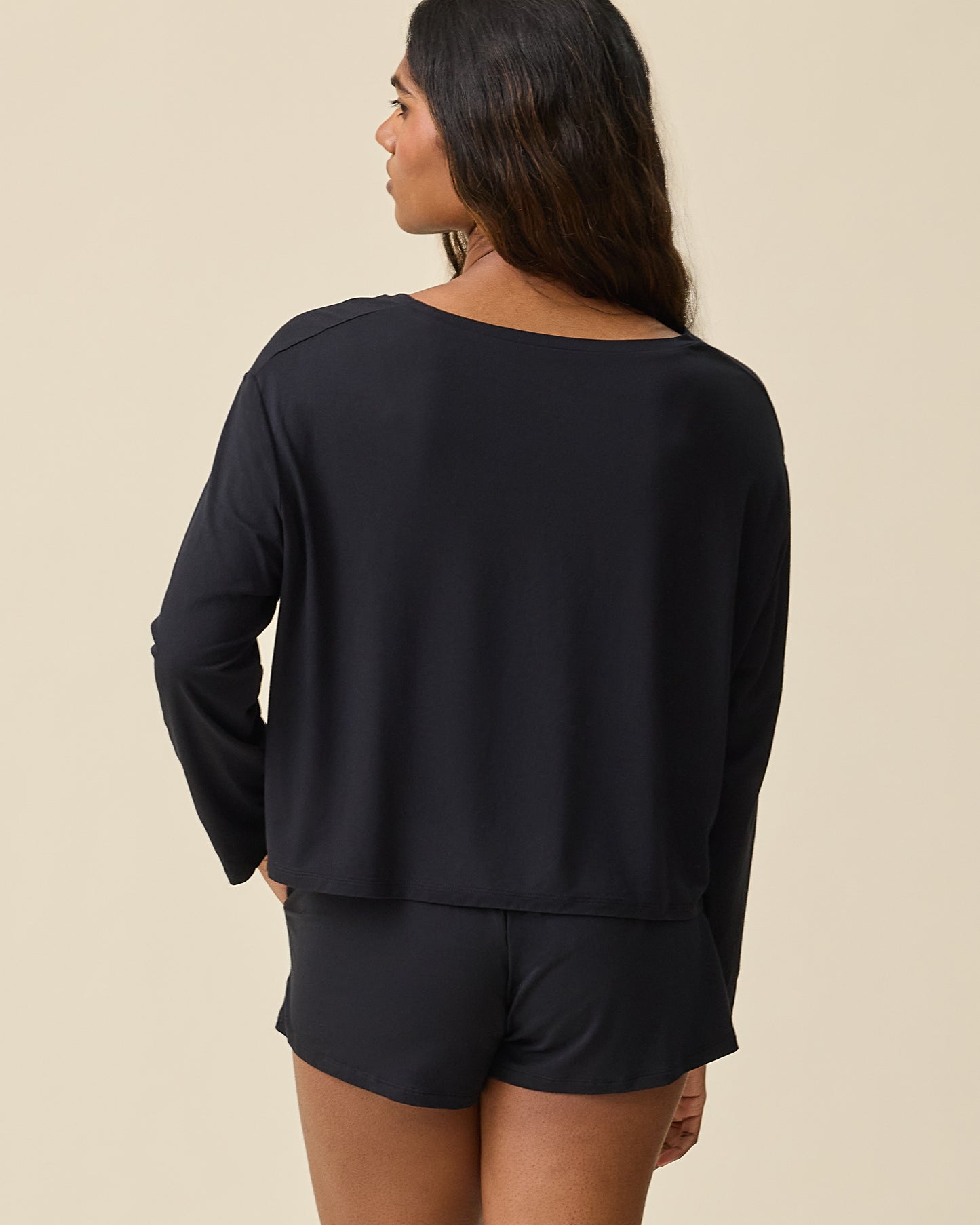 Woman wearing the Aria Bamboo Casual Cropped Long Sleeve Top in black with matching shorts on a beige background