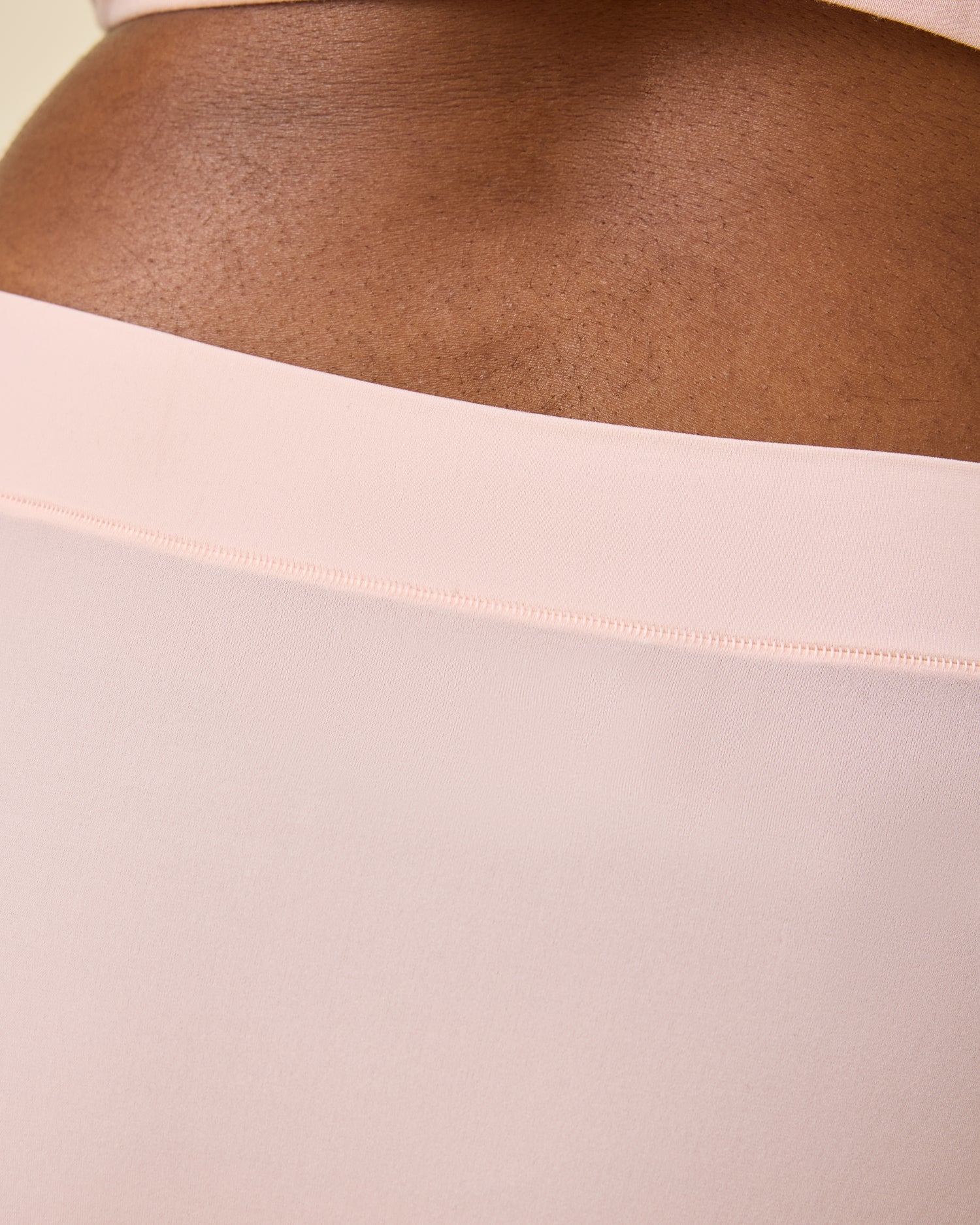Close up of model wearing Grow with Me™ Maternity & Postpartum Brief in Soft Pink  on a beige background