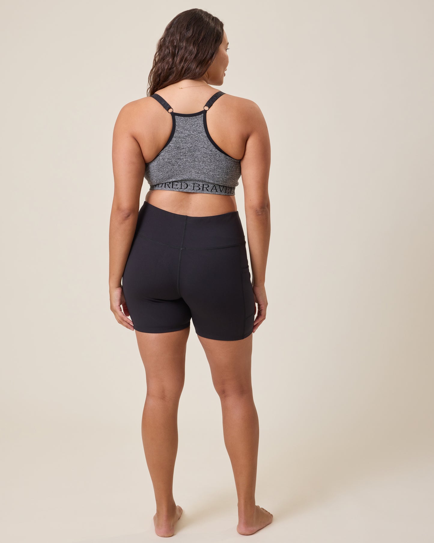 Woman wearing a gray sports bra and Stevie Active Postpartum Bike Short in black on a beige background