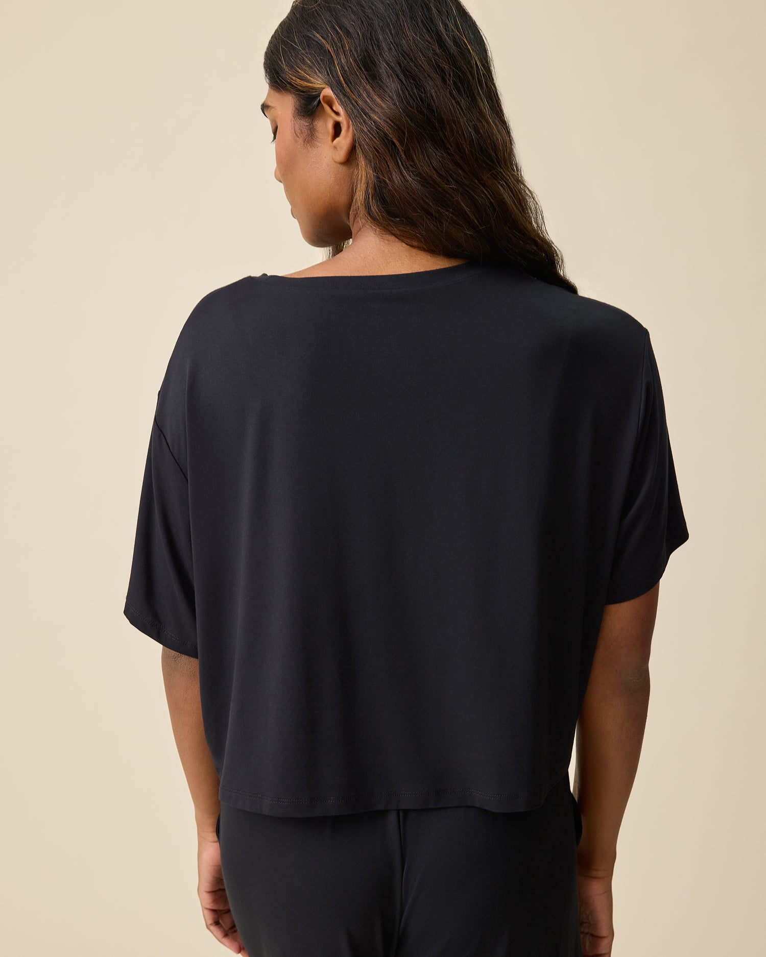 Woman wearing the Aria Bamboo Casual Cropped Short Sleeve Top in black with matching bottoms on beige background