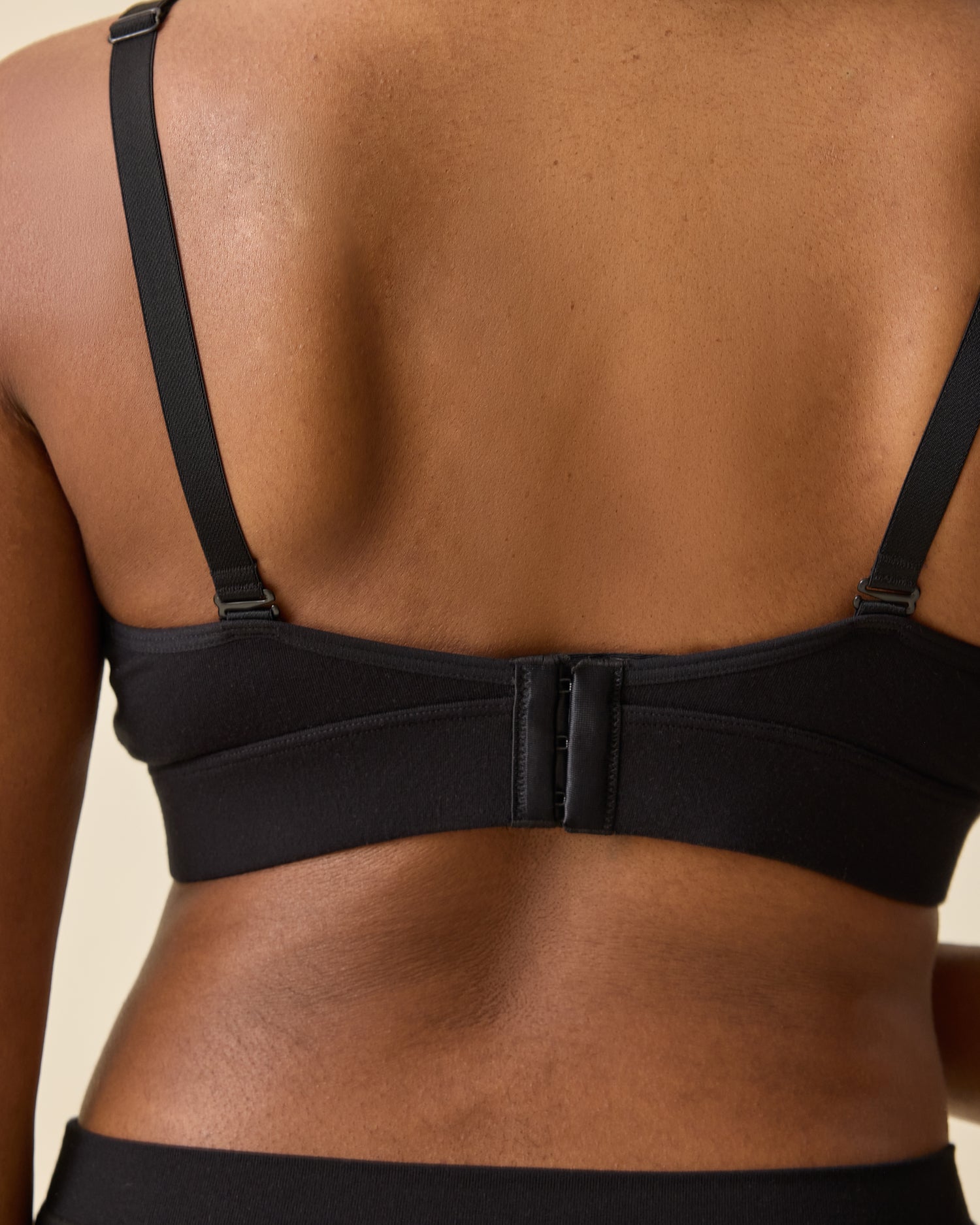 Back view of model wearing Every Stage Nursing Bra in Black on a beige background 