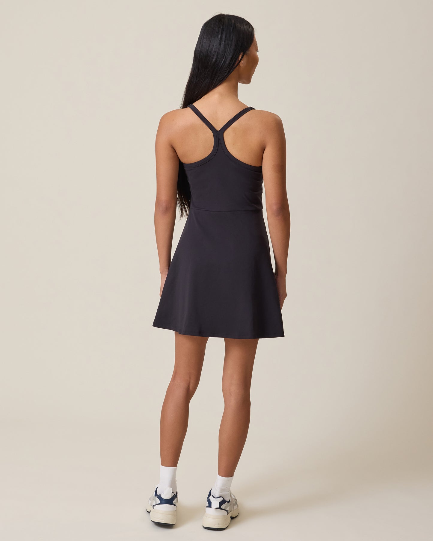 Woman wearing a black Stevie Racerback Nursing Dress with thin straps on a beige background