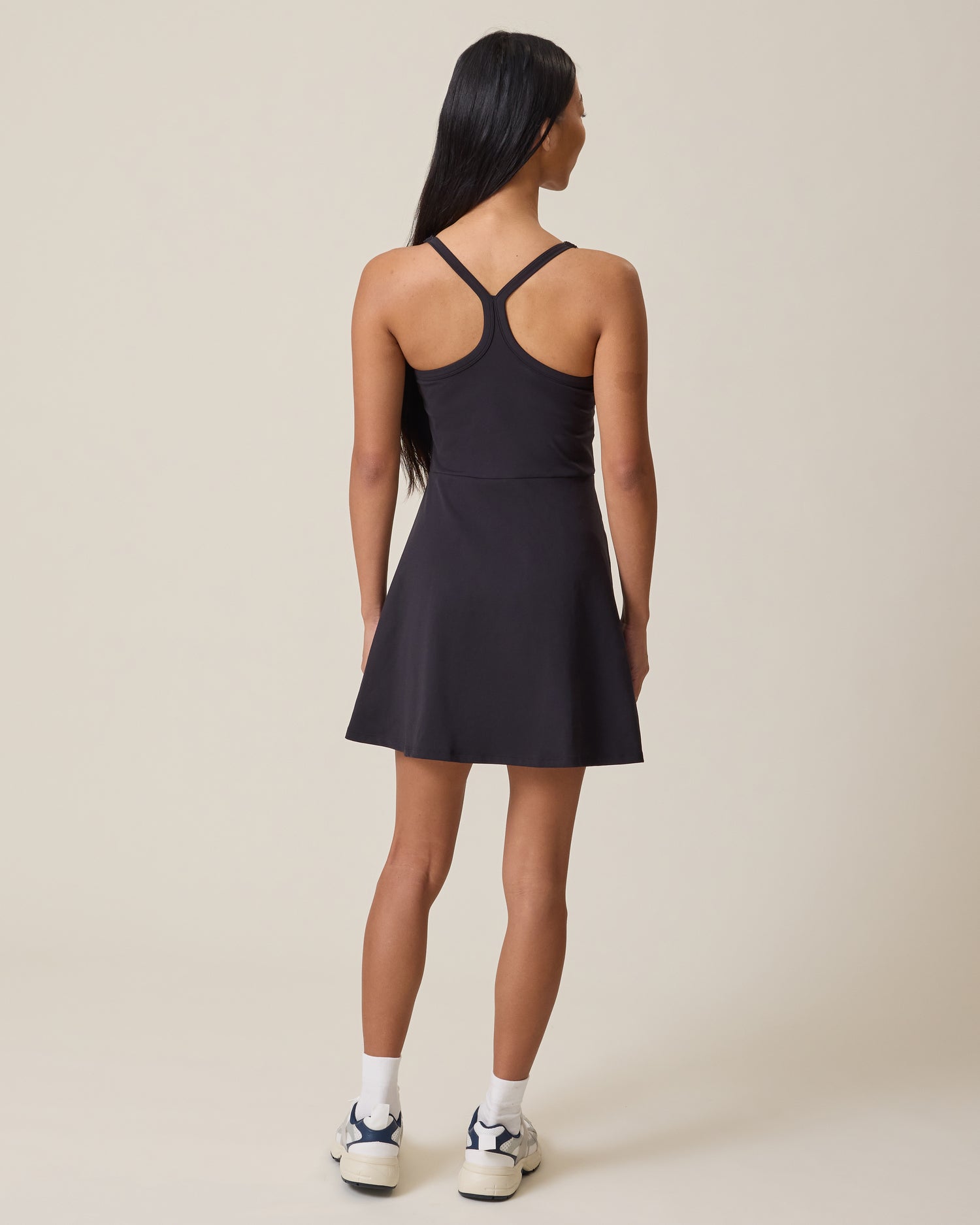 Woman wearing a black Stevie Racerback Nursing Dress with thin straps on a beige background