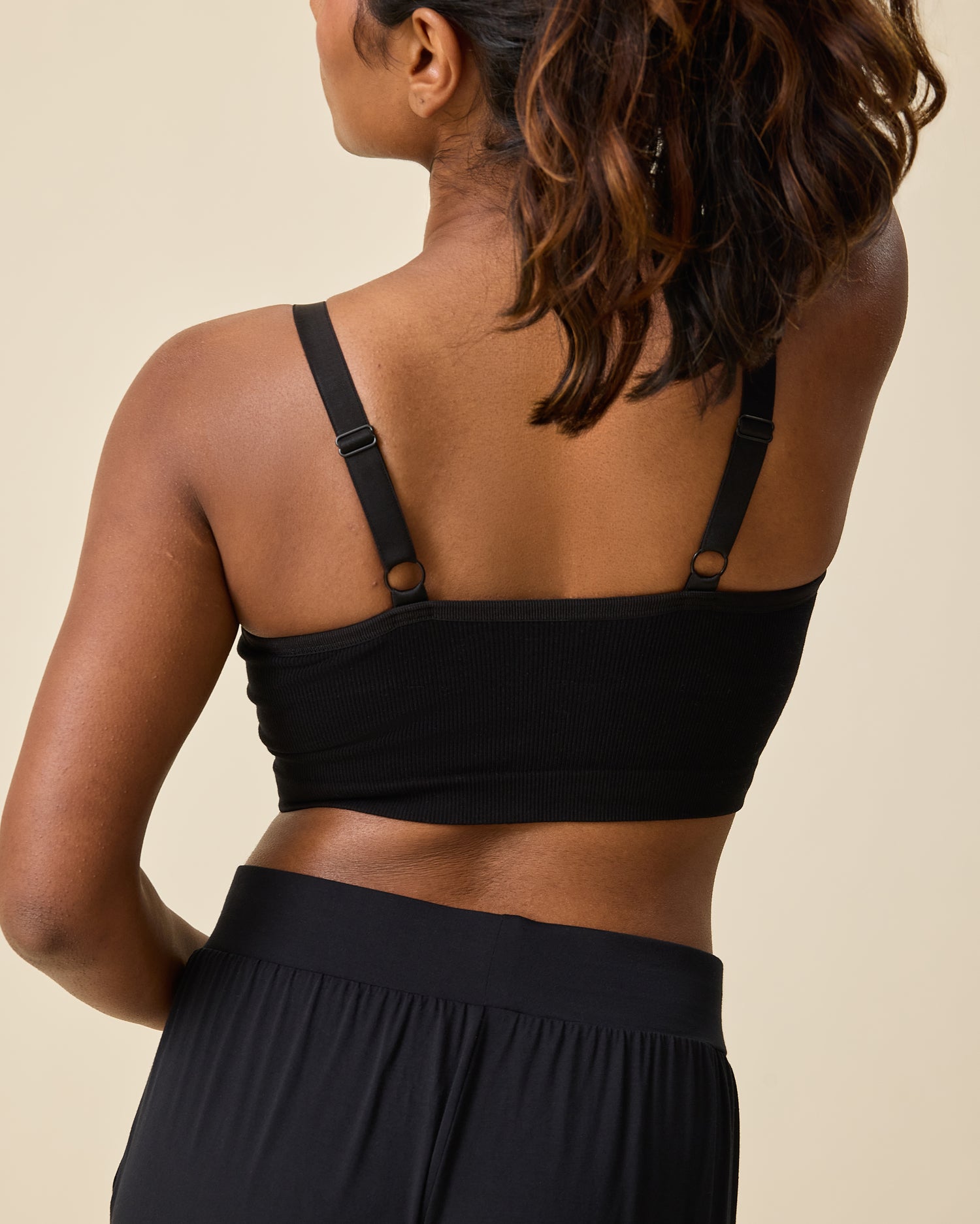 Back view of model wearing Sublime® Bamboo Hands-Free Pumping Lounge & Sleep Bra in Black on a beige background.