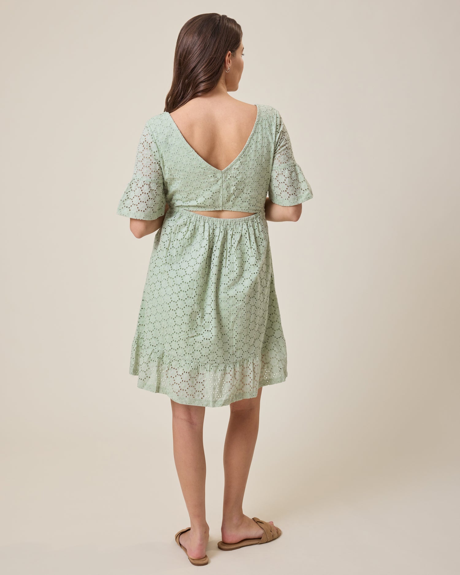 Woman wearing the Dahlia Eyelet Maternity & Nursing Dress in aqua mist with a subtle pattern on a beige background