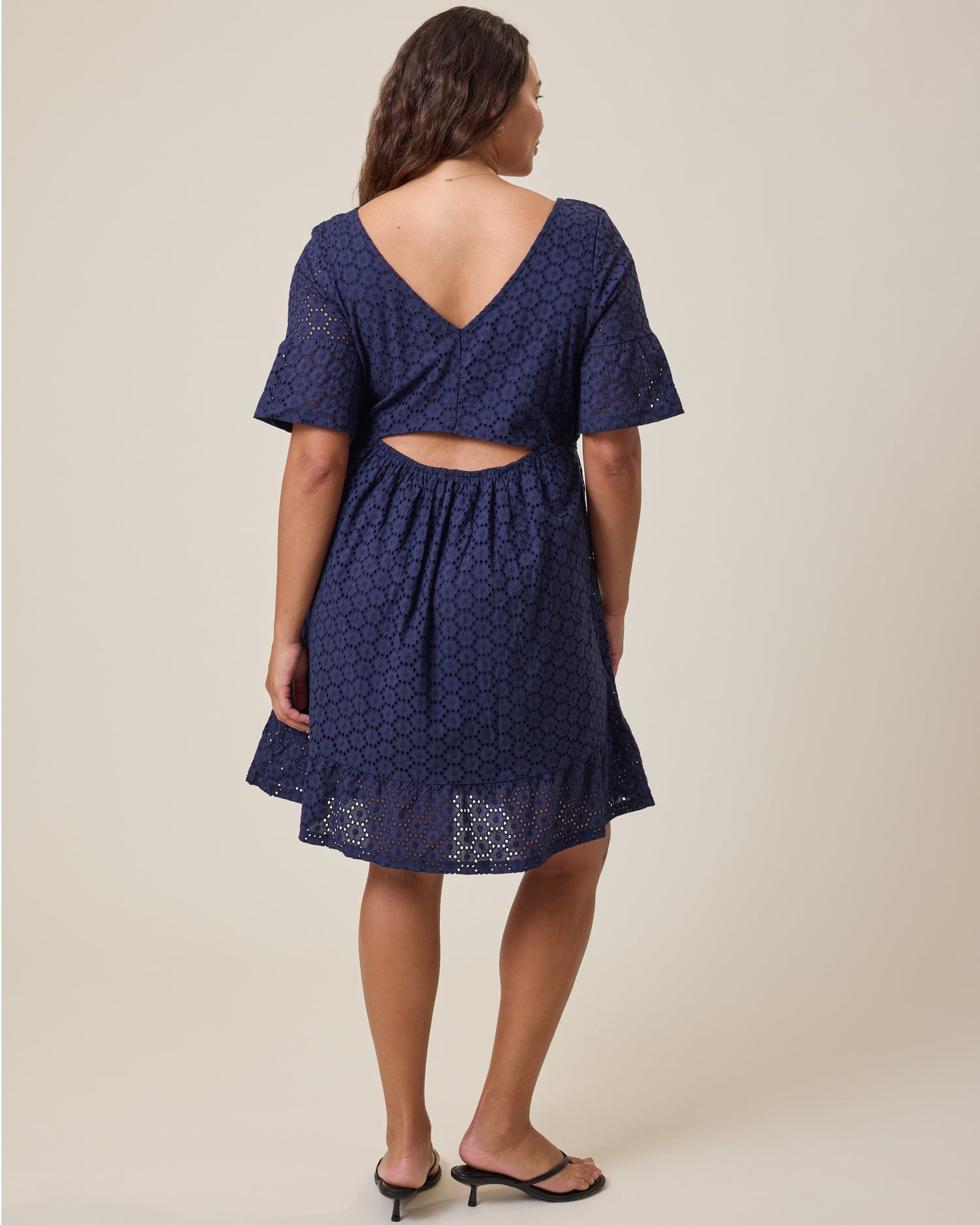 Woman wearing Dahlia Eyelet Maternity & Nursing Dress in Navy with cut-out design on a beige background