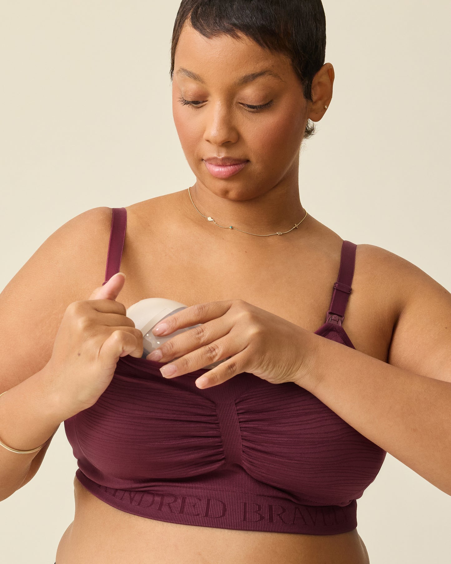 Model is displaying pumping access on  Sublime® Hands-Free Pumping & Nursing Bra in Deep Burgundy, on a beige background.