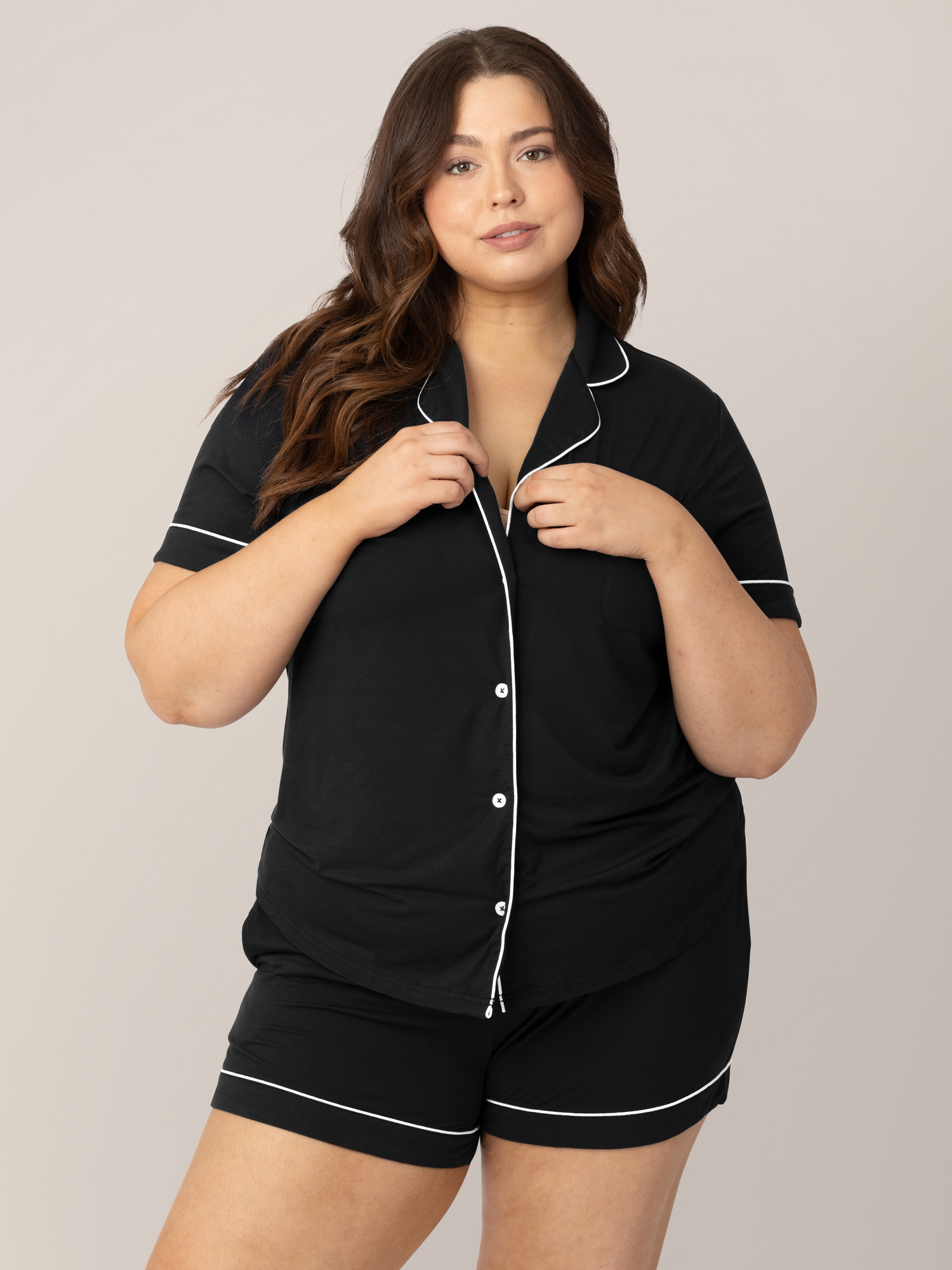 Model wearing the Clea Bamboo Short Sleeve Pajama Set in Black with her hands on her collar. 