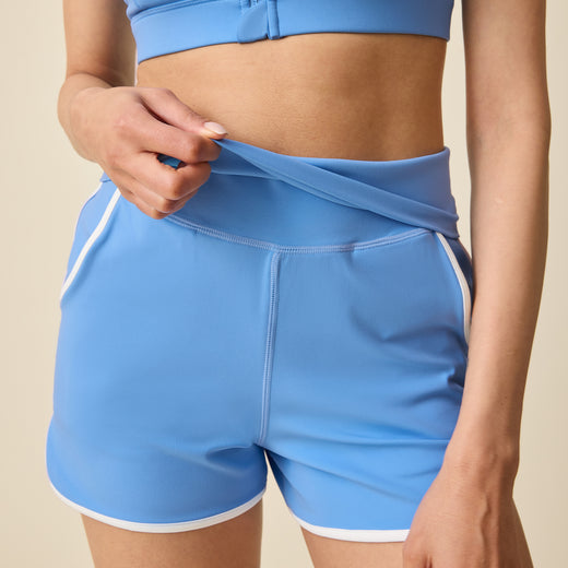 Model is displaying the foldable waistband on the Active Maternity & Postpartum Short - and High Impact Nursing Sports Bra in Harbor Blue on a beige background@model_info:Devyn is 5'7