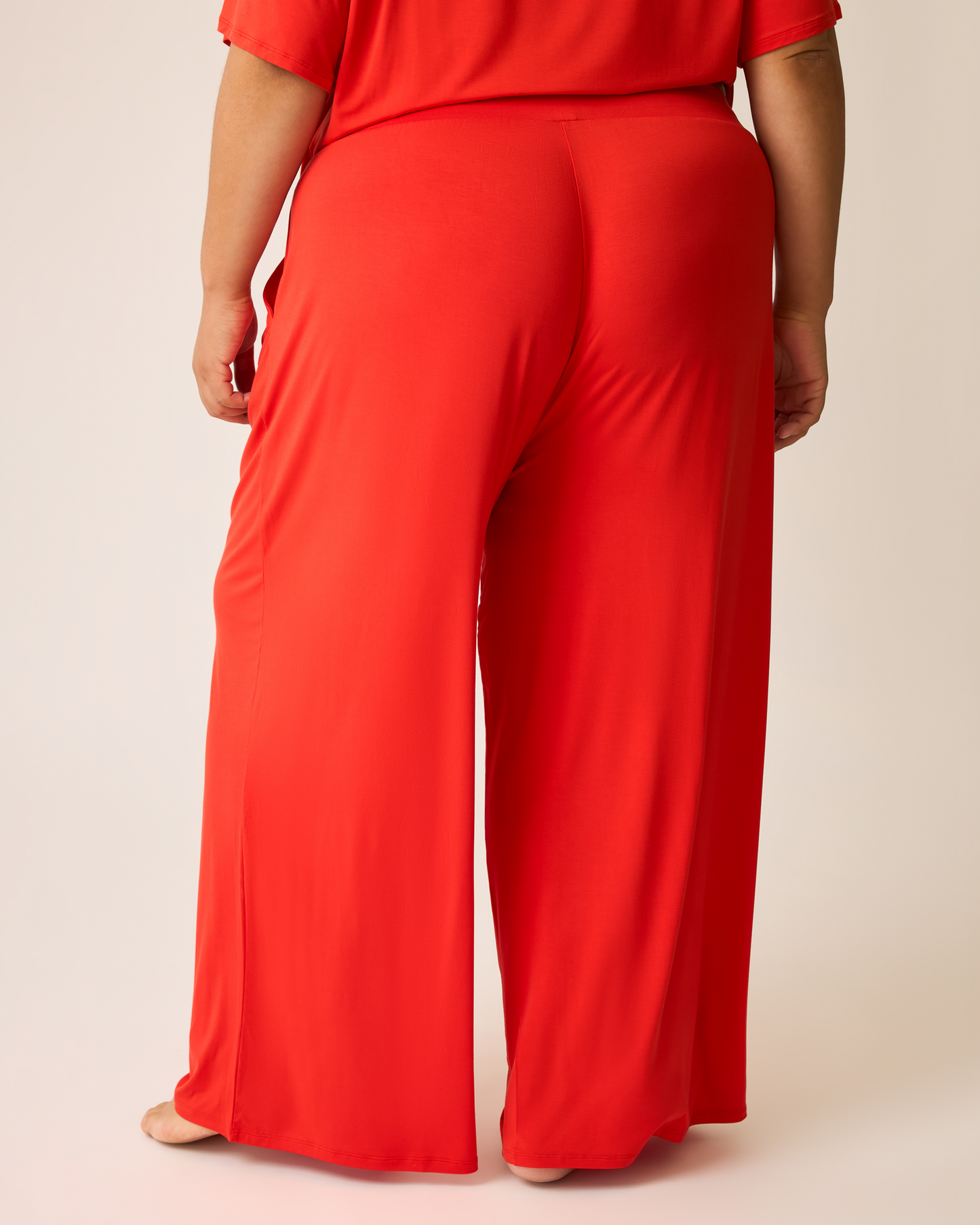 Person wearing a bright red Aria lounge outfit with wide-leg pants on a beige background