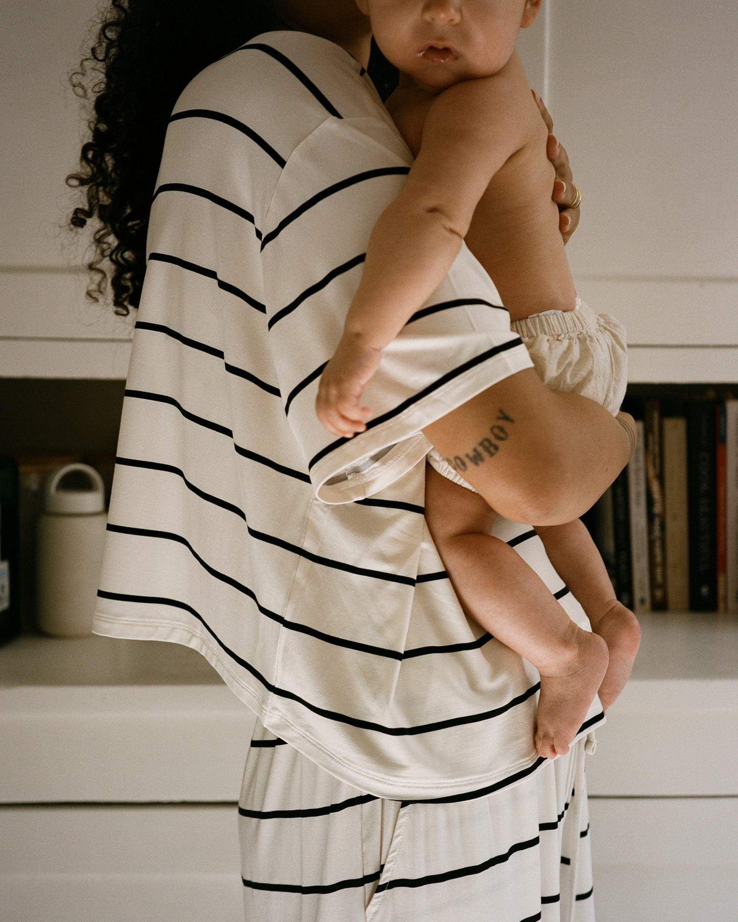 Person wearing a white and black striped lounge set holding a baby.@model_info:Natasha is wearing a Small.