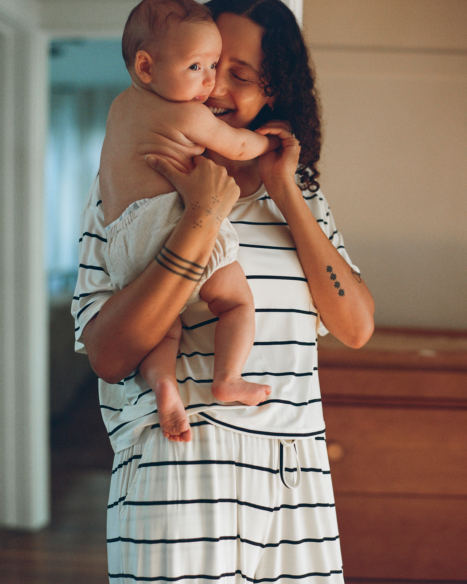 Woman in a striped lounge set holding a baby indoors @model_info:Natasha is 5'9" and wearing a Small.