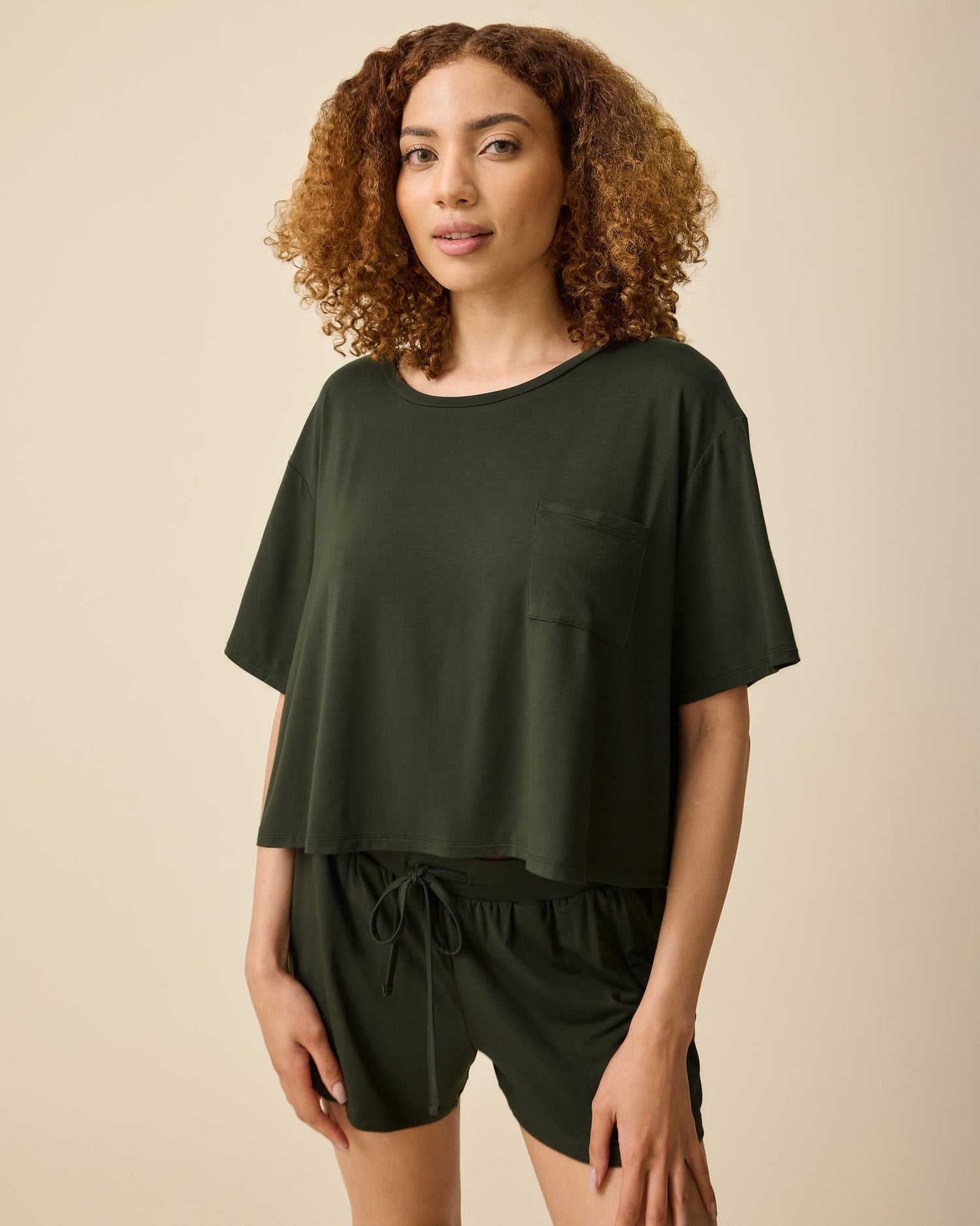 Model is wearing Aria Bamboo Casual Cropped Short Sleeve Top in Thyme and Aria Bamboo Casual Lounge Short in Thyme on a beige background.@model_info:Devyn is wearing a Small.