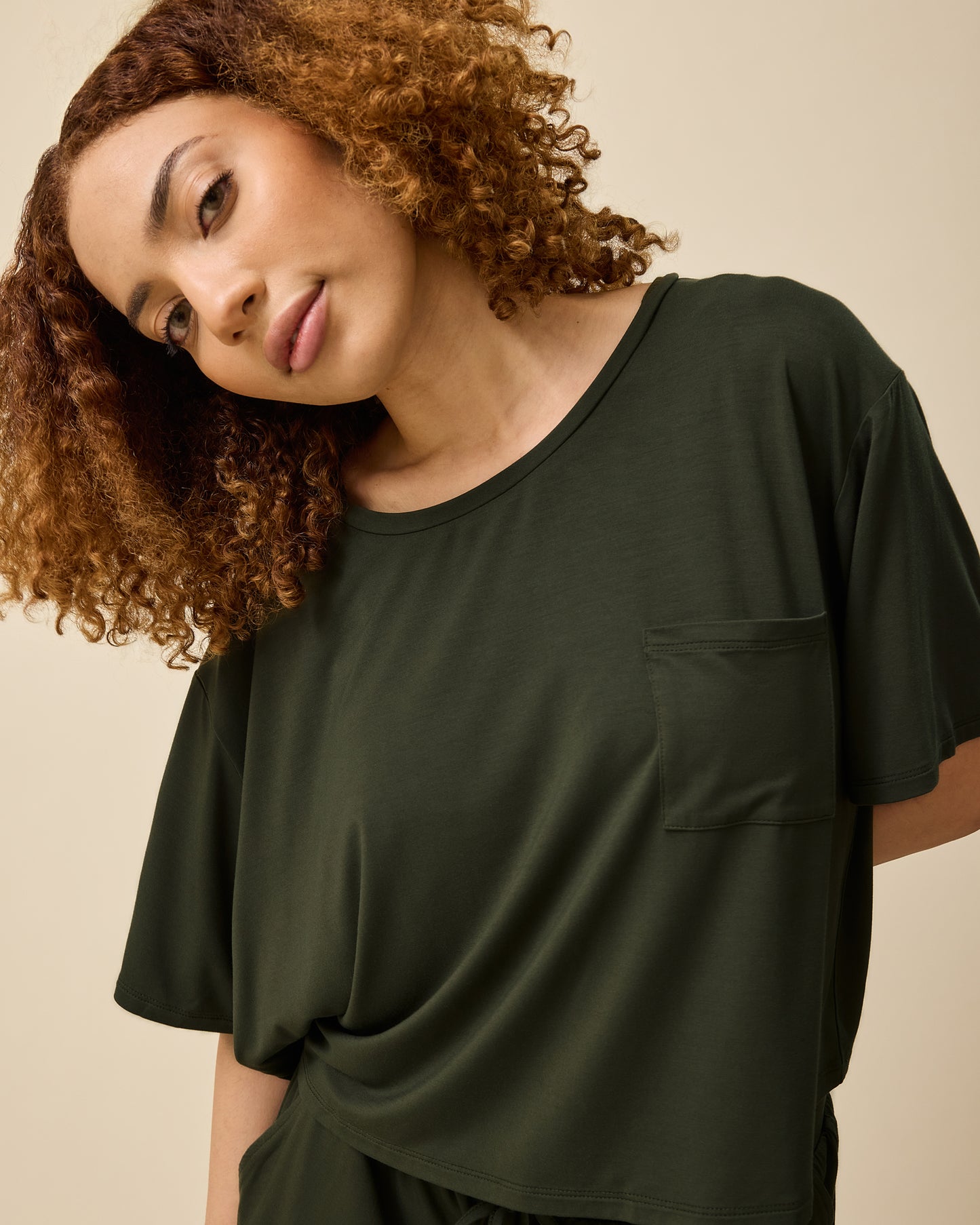 Model is wearing Aria Bamboo Casual Cropped Short Sleeve Top in Thyme and Aria Bamboo Casual Lounge Short in Thyme on a beige background.