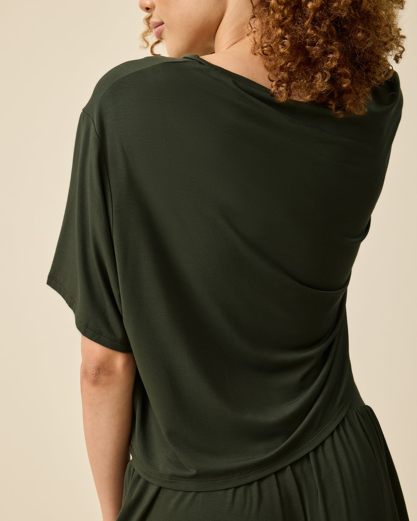 Back view of model wearing Aria Bamboo Casual Cropped Short Sleeve Top in Thyme and Aria Bamboo Casual Lounge Short in Thyme on a beige background.