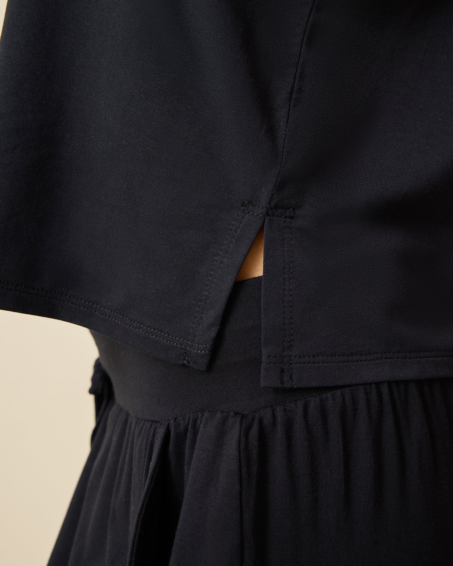 Close up of side view of model wearing Aria Bamboo Cropped V-neck Tank in Black and Aria Bamboo Casual Lounge Pant in Black on a beige background.