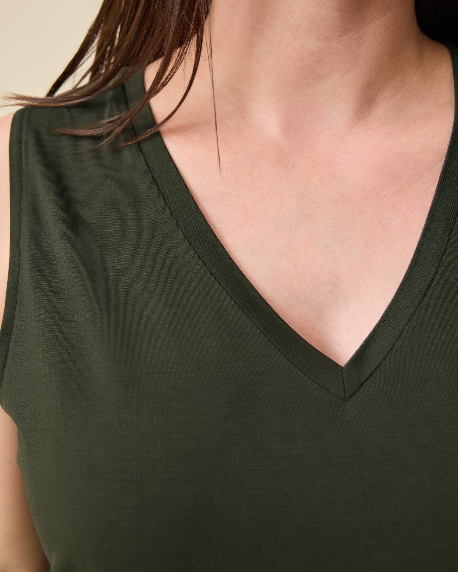 Close up of Model wearing Aria Bamboo Cropped V-neck Tank in Thyme on a beige background.
