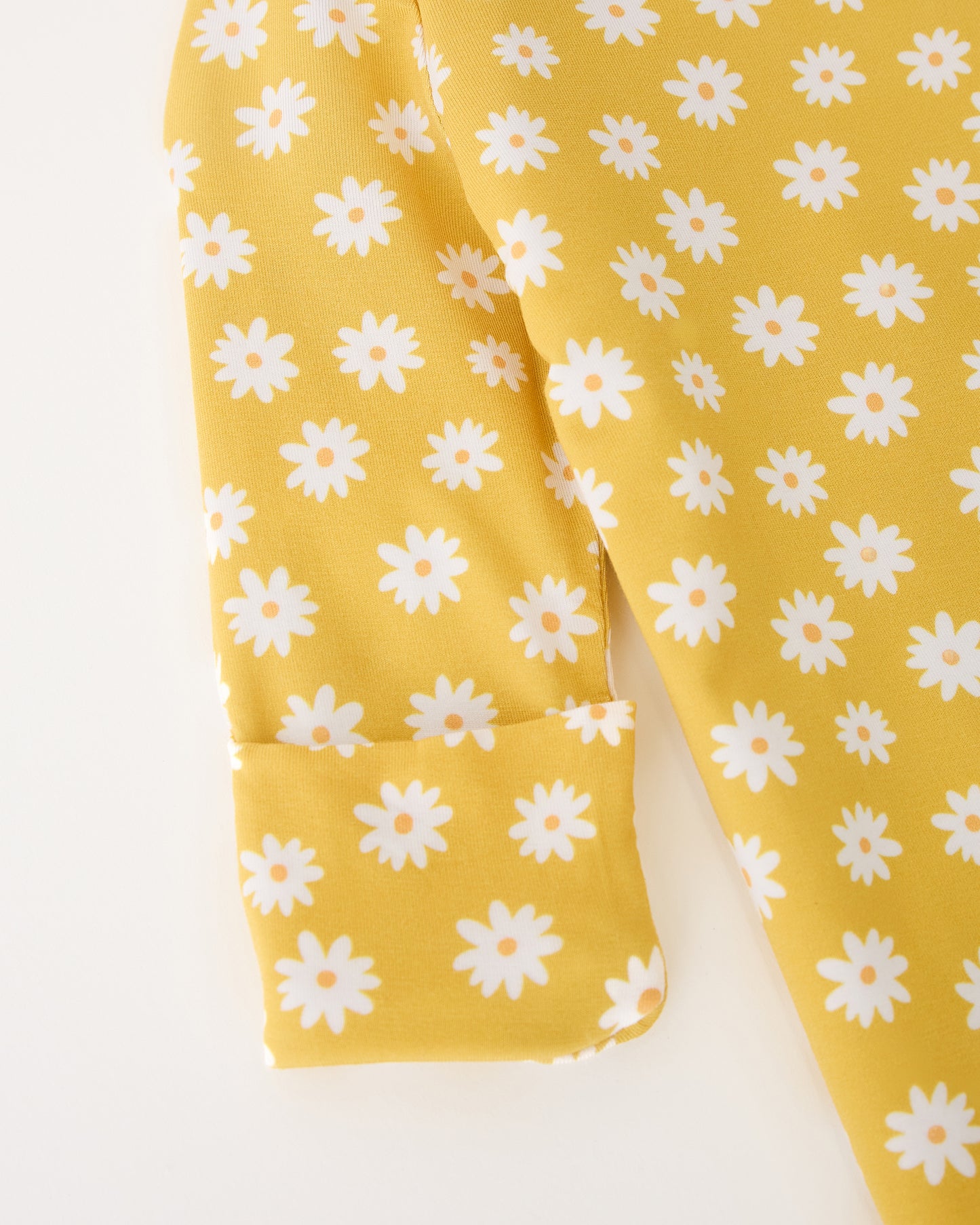 Close up of the sleeve detail of the Bamboo Knotted Baby Gown & Hat in Yellow Daisies on a beige background