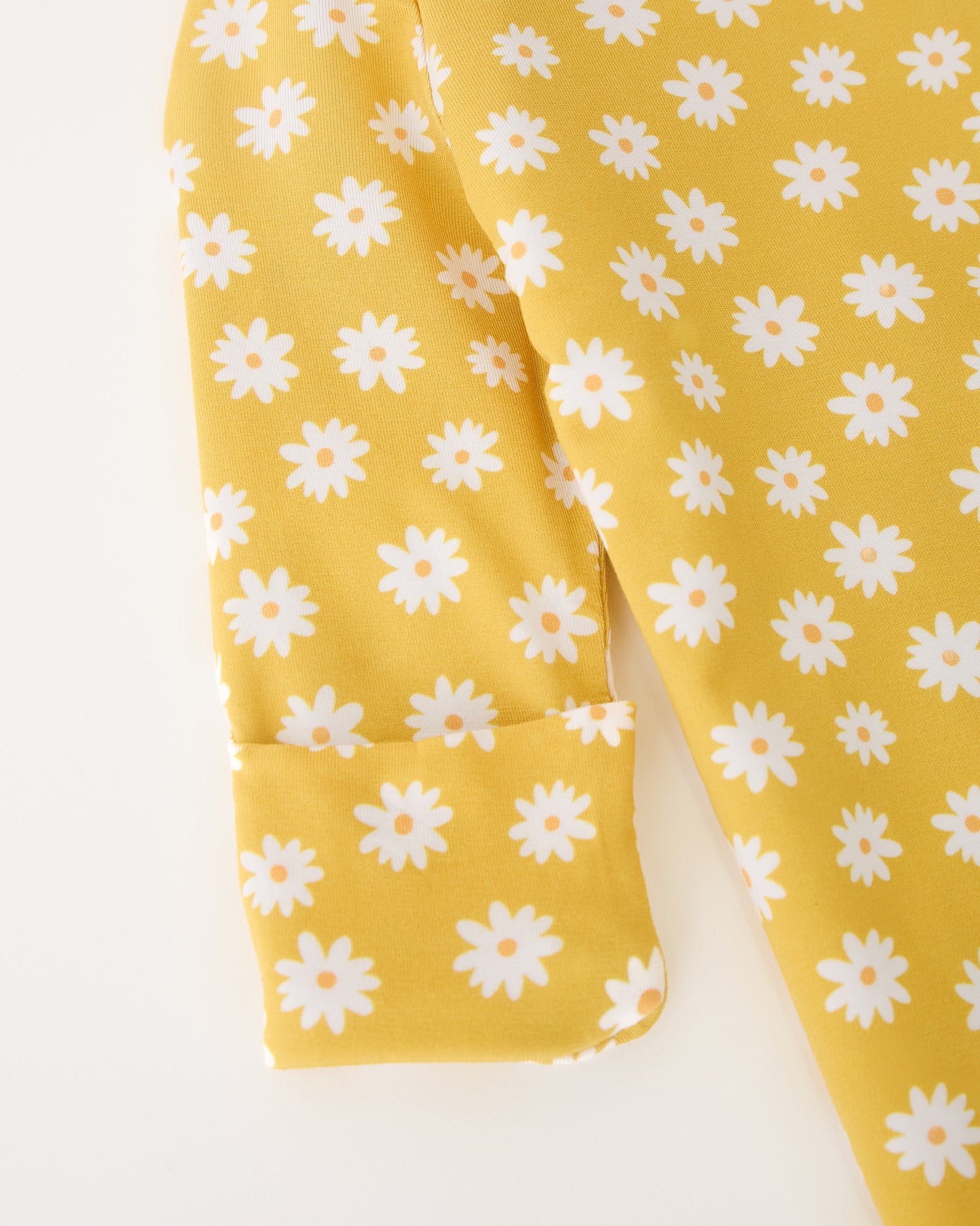 Close up of the sleeve detail of the Bamboo Knotted Baby Gown & Hat in Yellow Daisies on a beige background