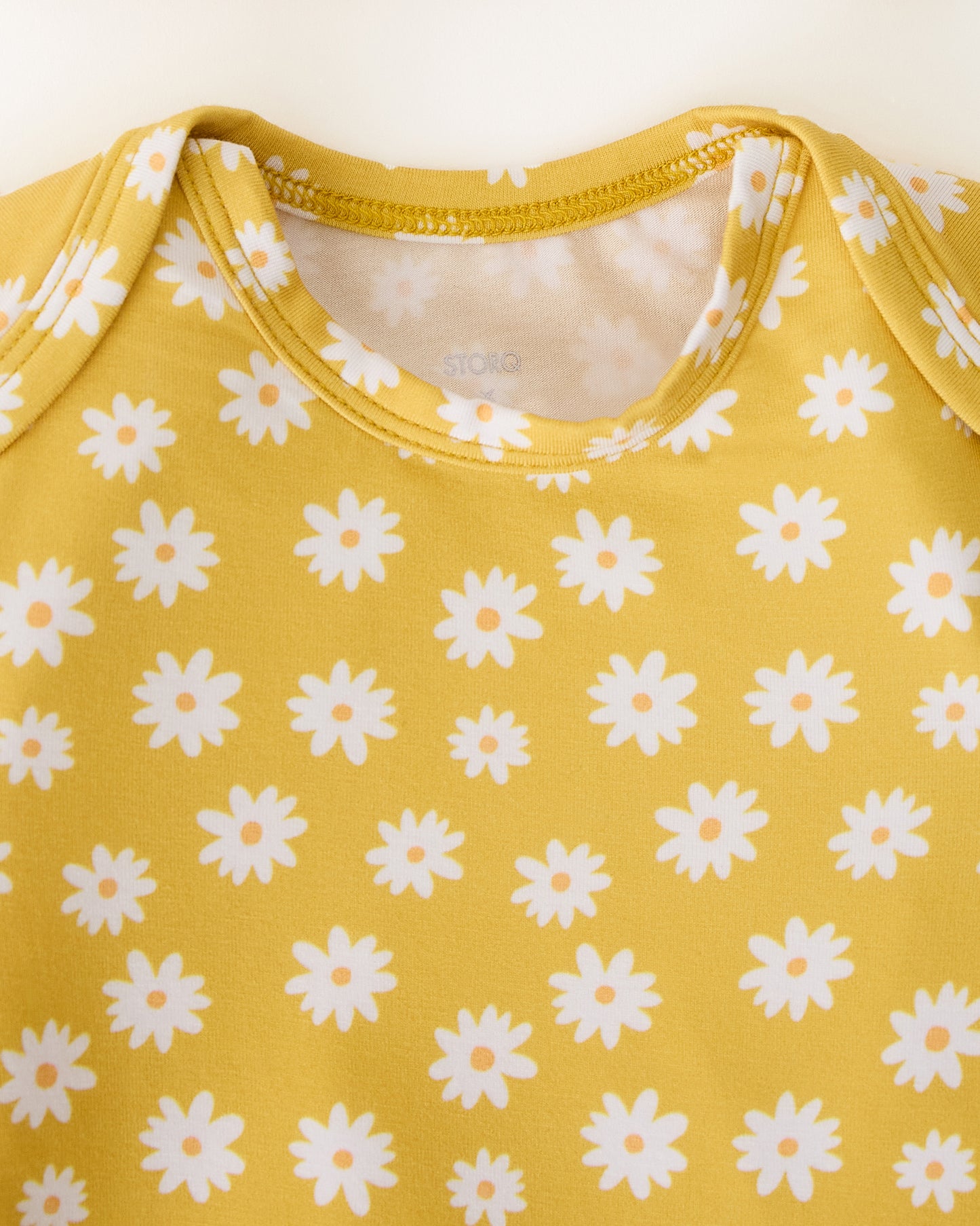 Close up of the neckline detail of the Bamboo Knotted Baby Gown & Hat in Yellow Daisies on a beige background
