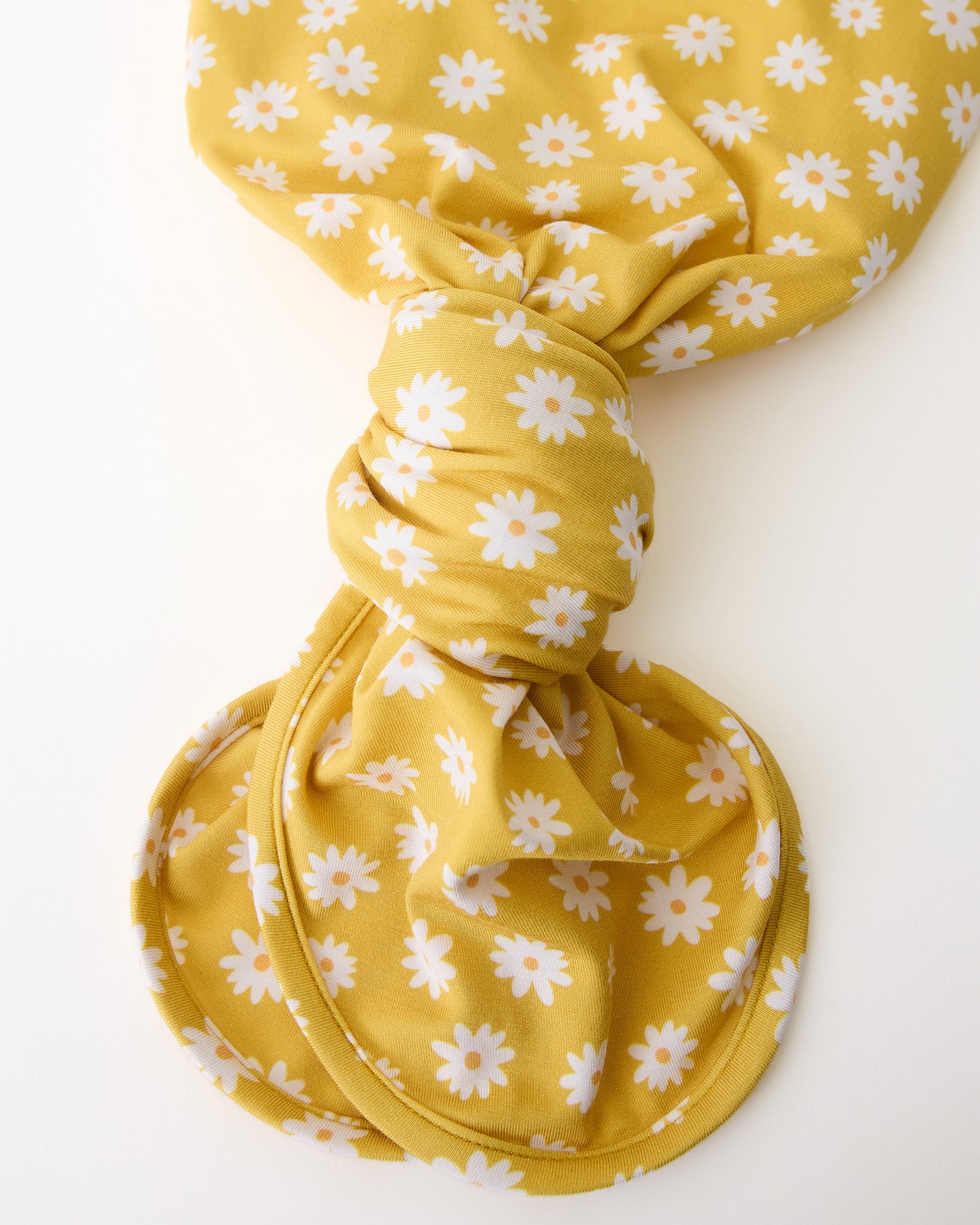 Close up of the knotted bottom of the Bamboo Knotted Baby Gown & Hat in Yellow Daisies on a beige background