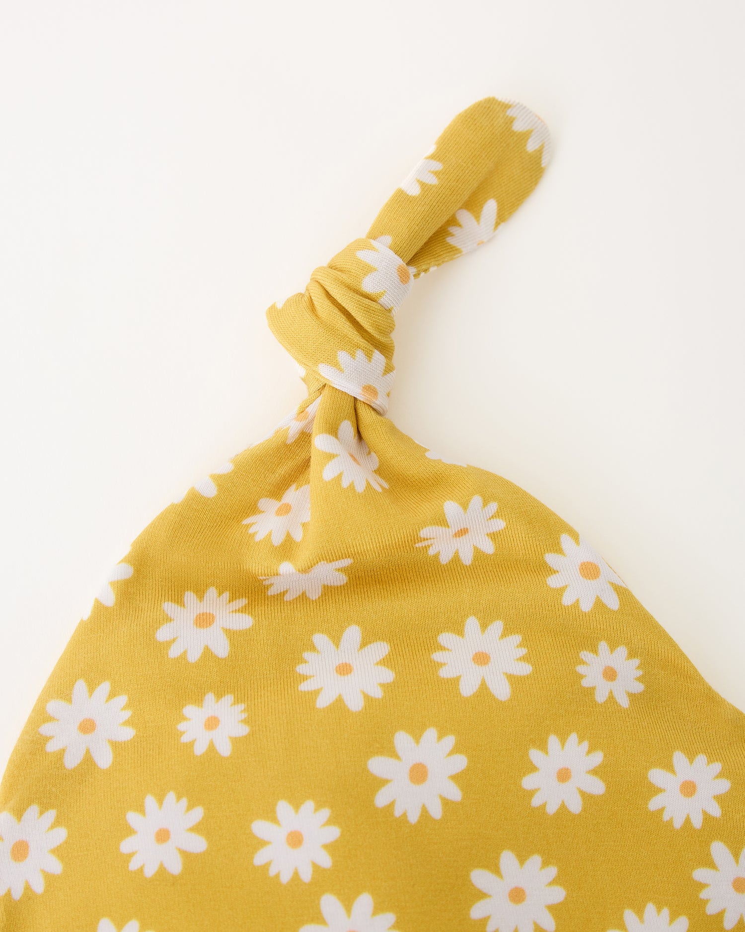Close up of the knotted hat top of the Bamboo Knotted Baby Gown & Hat in Yellow Daisies on a beige background