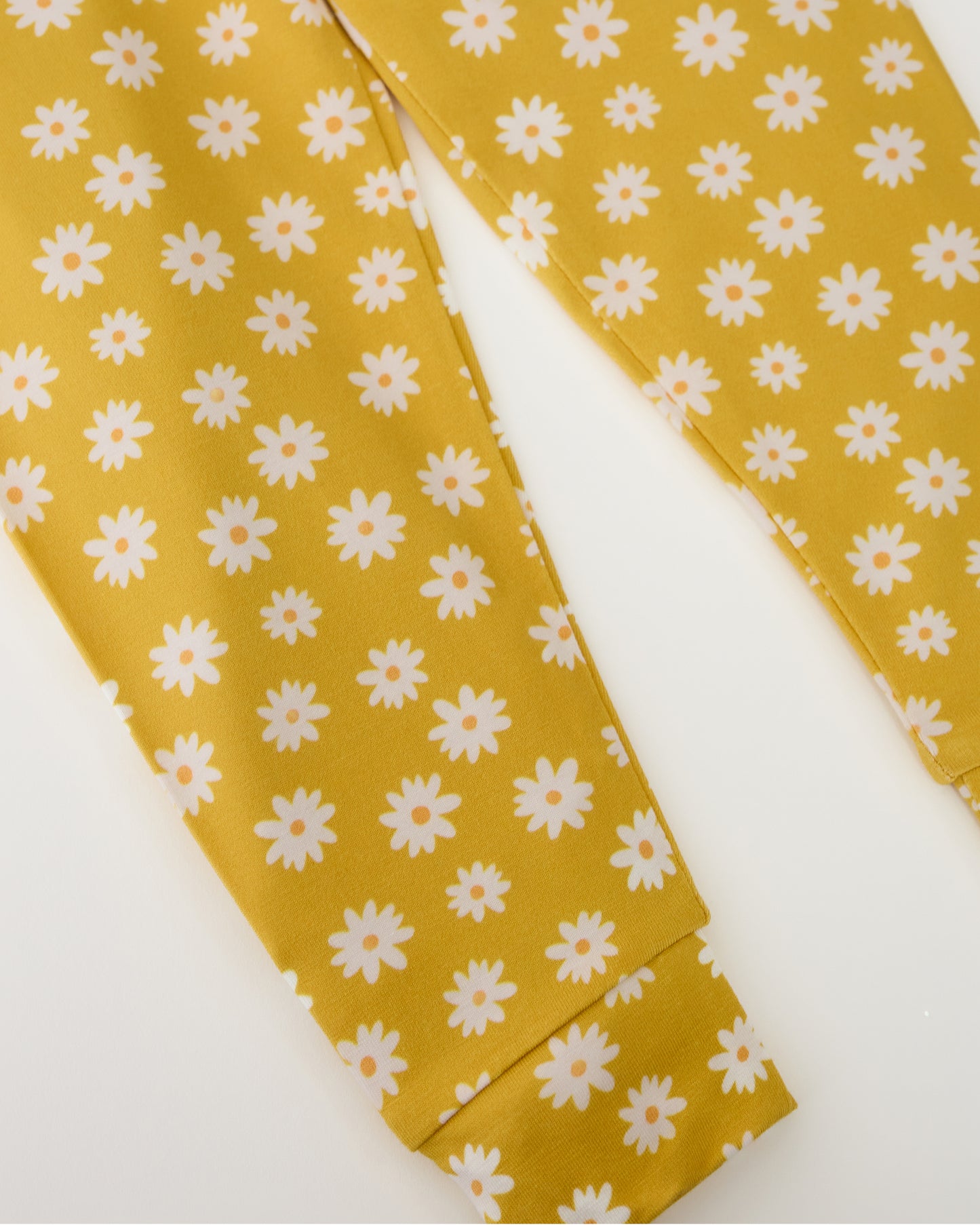 Close up of pants on Bamboo Baby Two-Piece Pajama Set in Yellow Daisies on a beige background