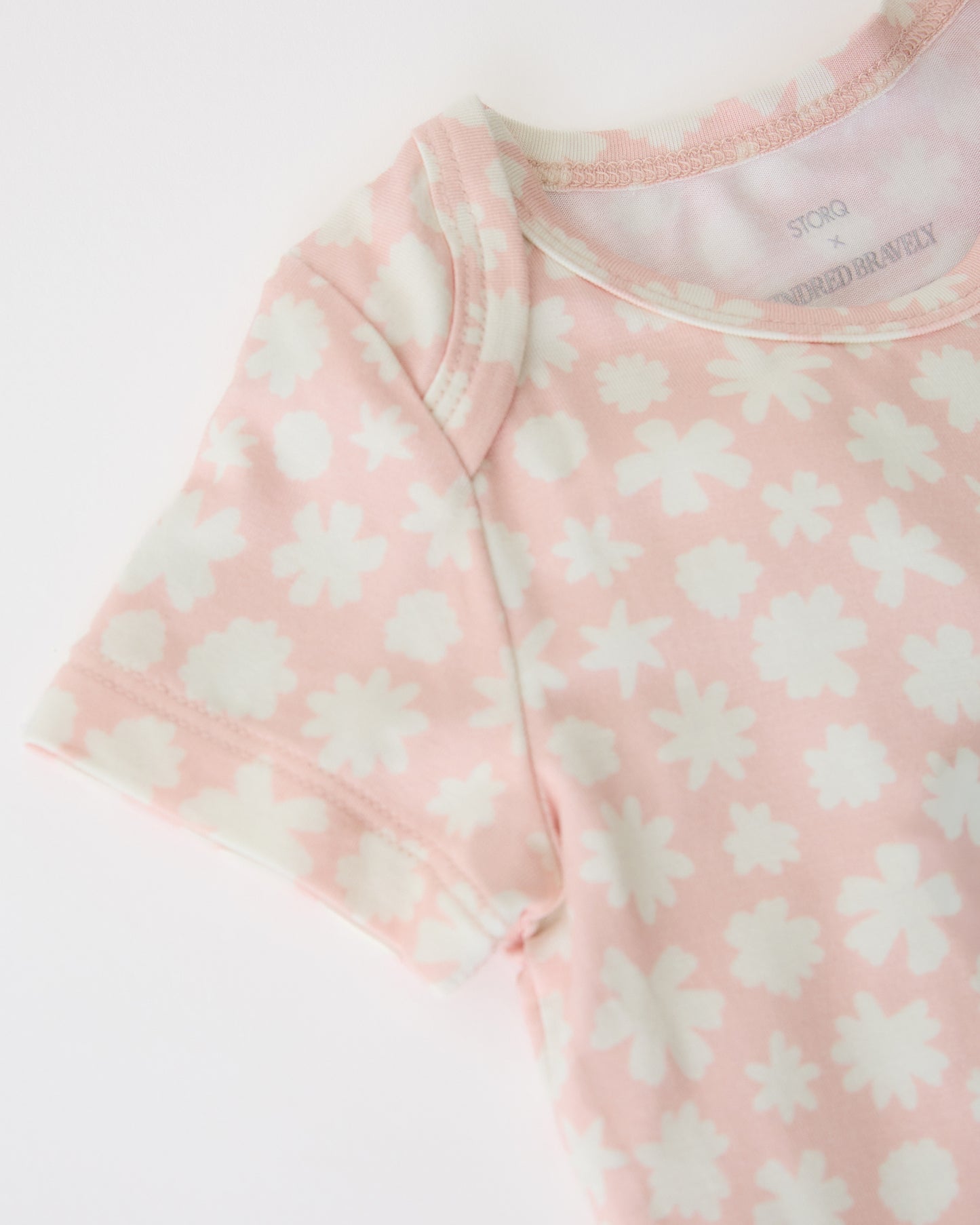 Close up of neckline and sleeve of Pink Chamomiles of the Baby Onesie Two-Pack in Cream & Pink Chamomiles on a beige background