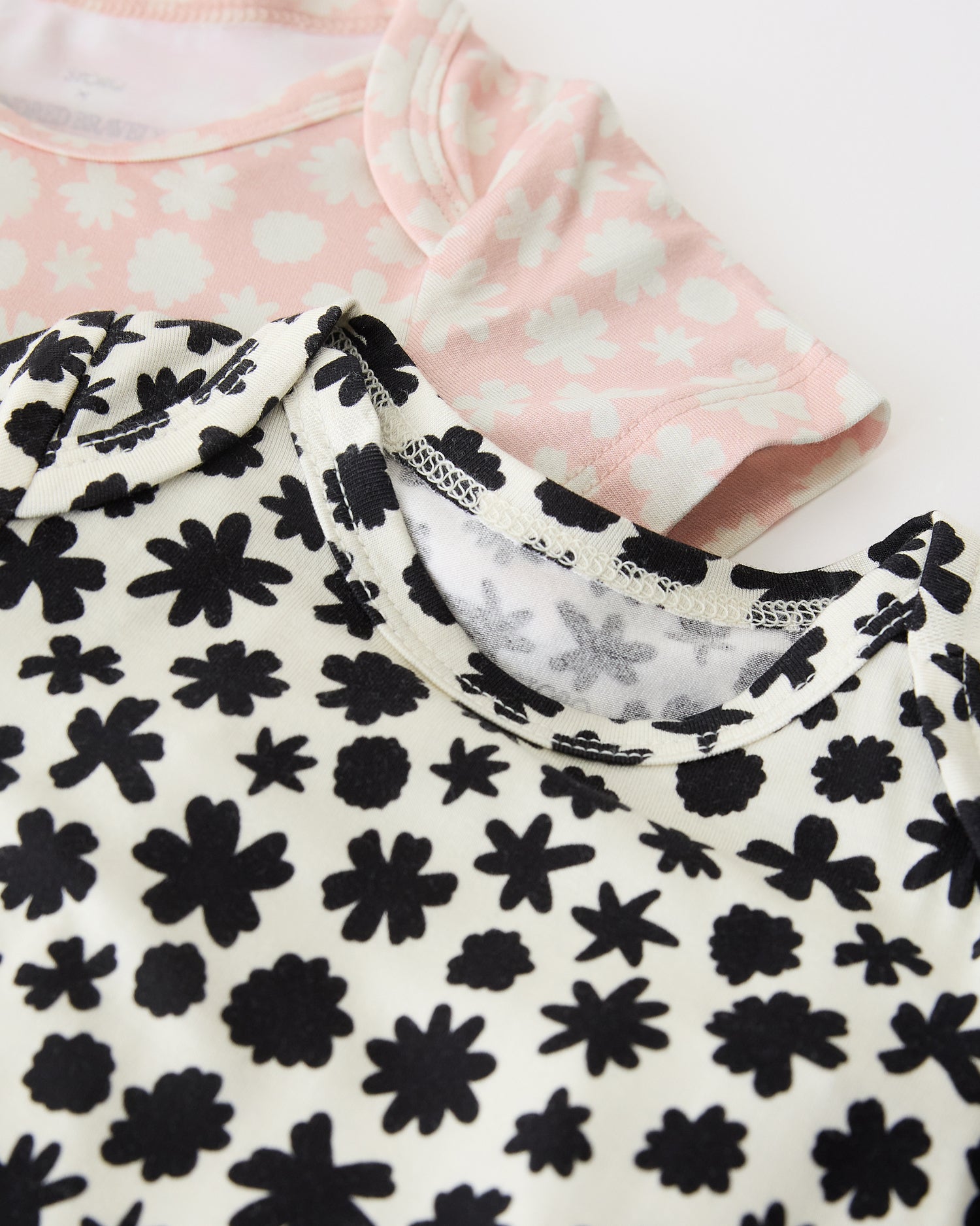 Close up of neckline of Baby Onesie Two-Pack in Cream & Pink Chamomiles on a beige background