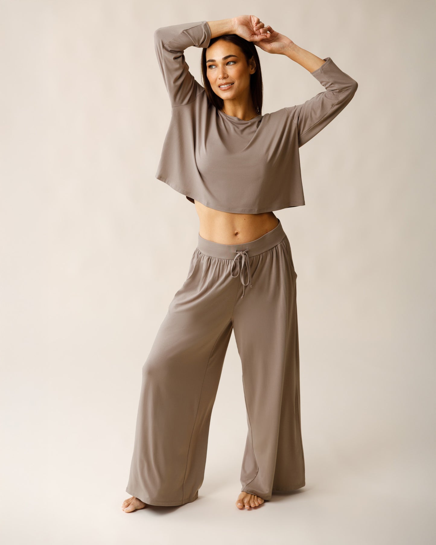 Woman wearing the Aria Bamboo Casual Lounge Pant in Taupe, paired with matching Aria Bamboo Casual Cropped Long Sleeve Top, with arms overhead@model_info:Lisa is 5'6" and wearing a Small.