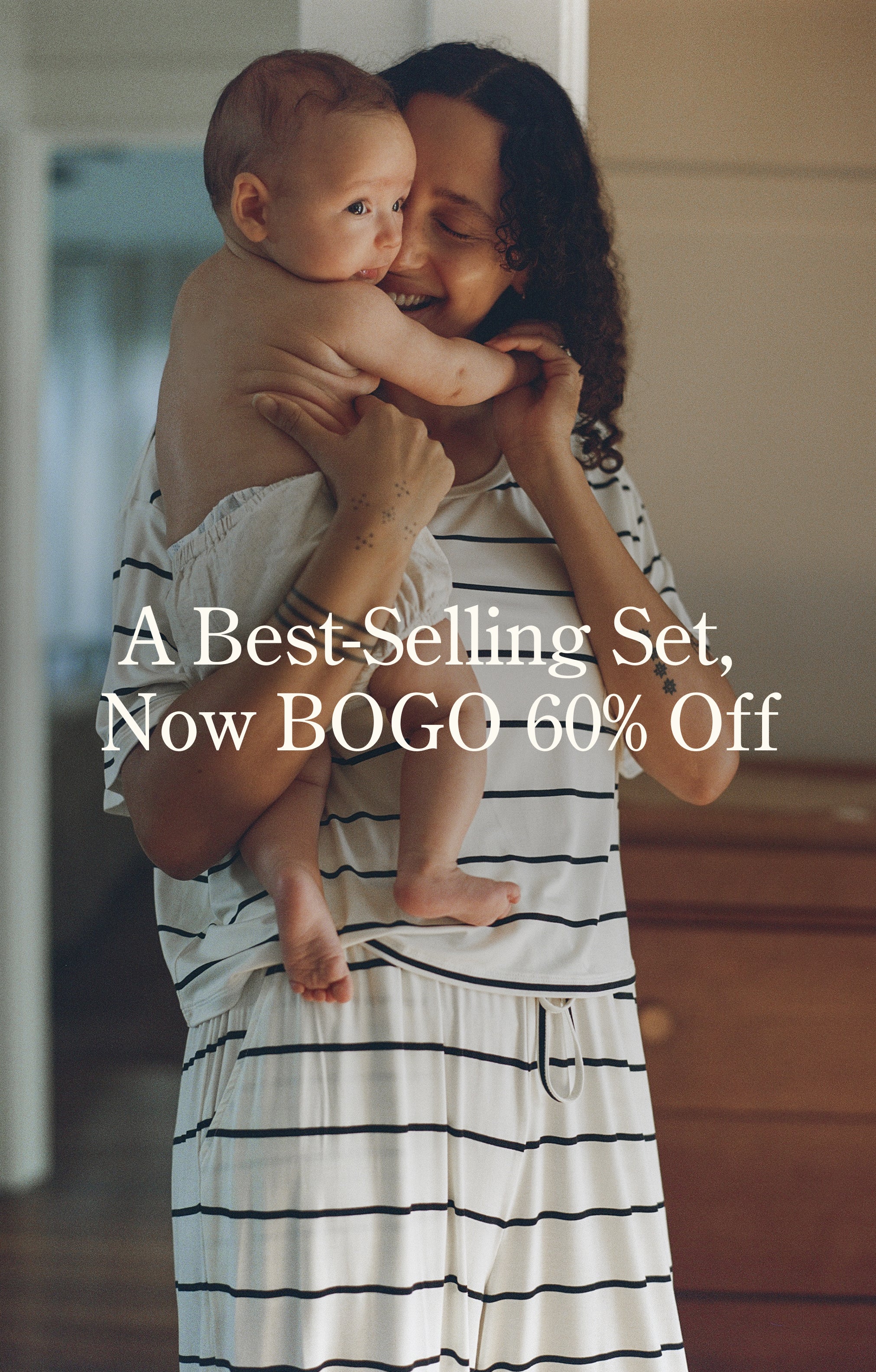 White text reads, A Best-Selling Set, Now BOGO 60% Off. Image of a mother holding and smiling at baby, and wearing Aria Bamboo Casual Lounge Pant and Aria Bamboo Casual Cropped Short Sleeve Top in White & Black Stripe on a warm home background.