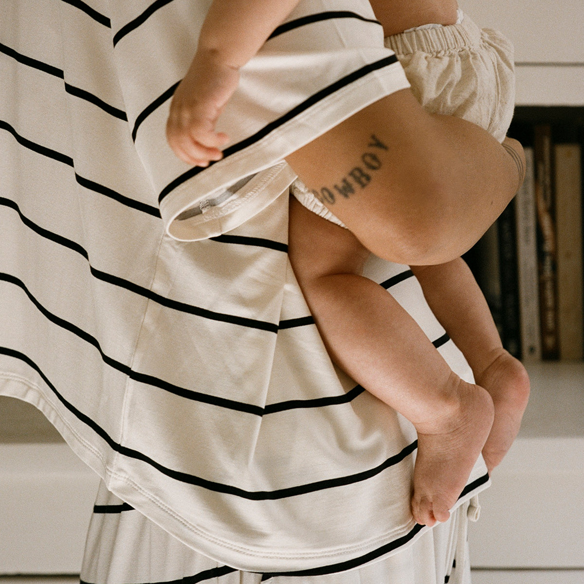 Mom holding baby near bookshelf while wearing Aria Bamboo Casual Cropped Short Sleeve Top and Aria Bamboo Casual Lounge Pant in White & Black Stripe.