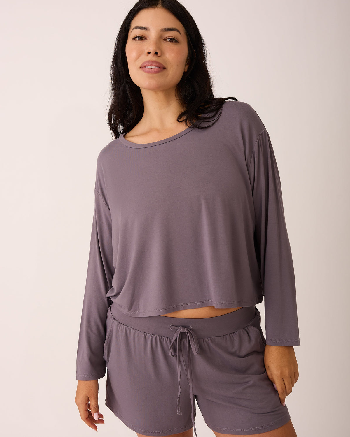 Model is wearing Aria Bamboo Casual Cropped Long Sleeve Top in Granite and Aria Bamboo Casual Lounge Short in Granite on a beige background.