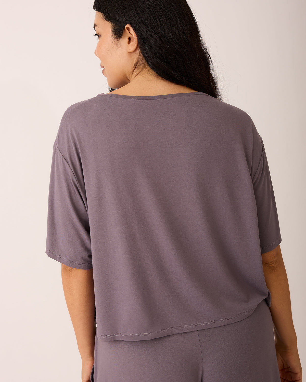 Back view of model wearing Aria Bamboo Casual Cropped Short Sleeve Top in Granite and Aria Bamboo Casual Lounge Pant in Granite on a beige background.