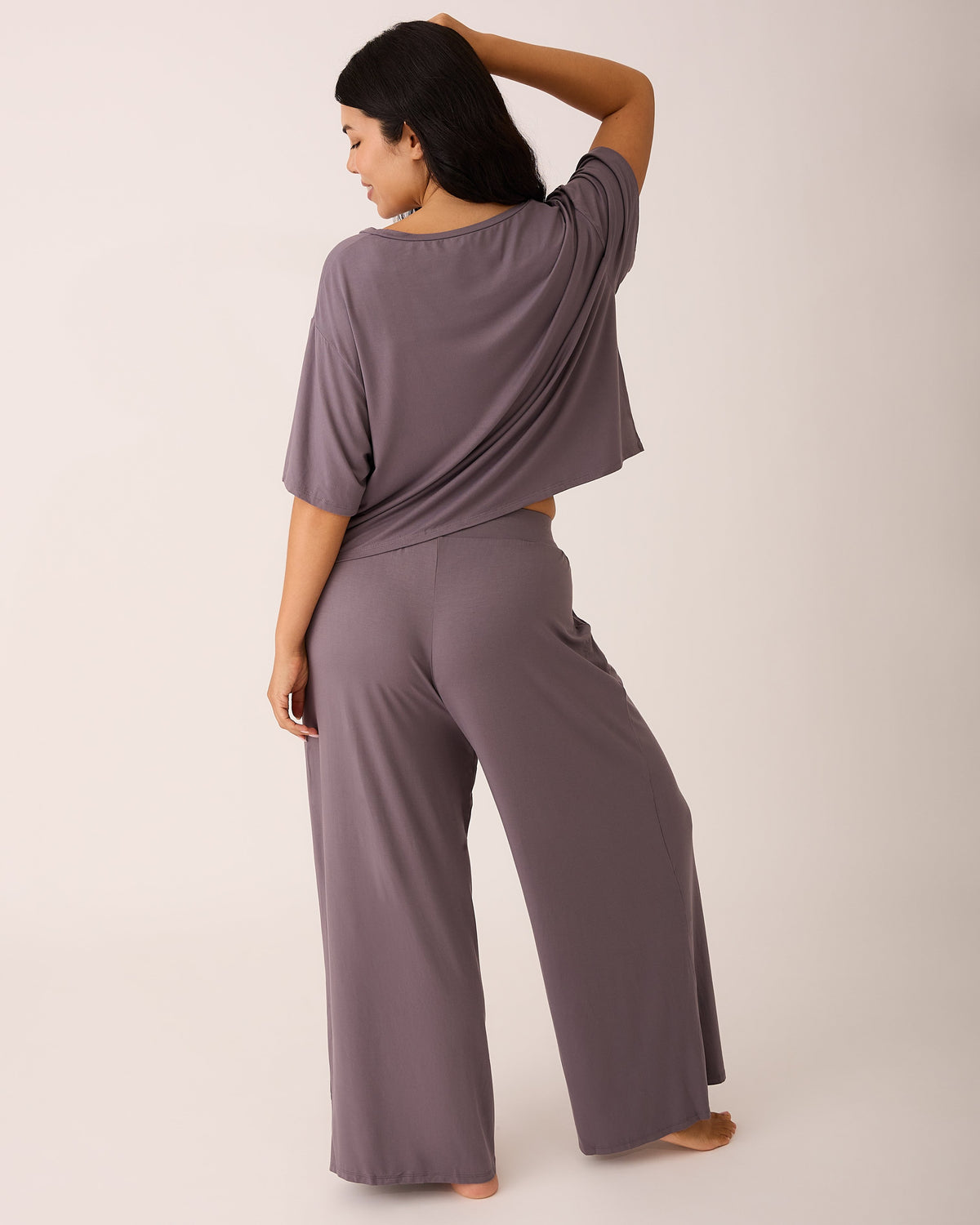Back view of model wearing Aria Bamboo Casual Cropped Short Sleeve Top in Granite and Aria Bamboo Casual Lounge Pant in Granite on a beige background.