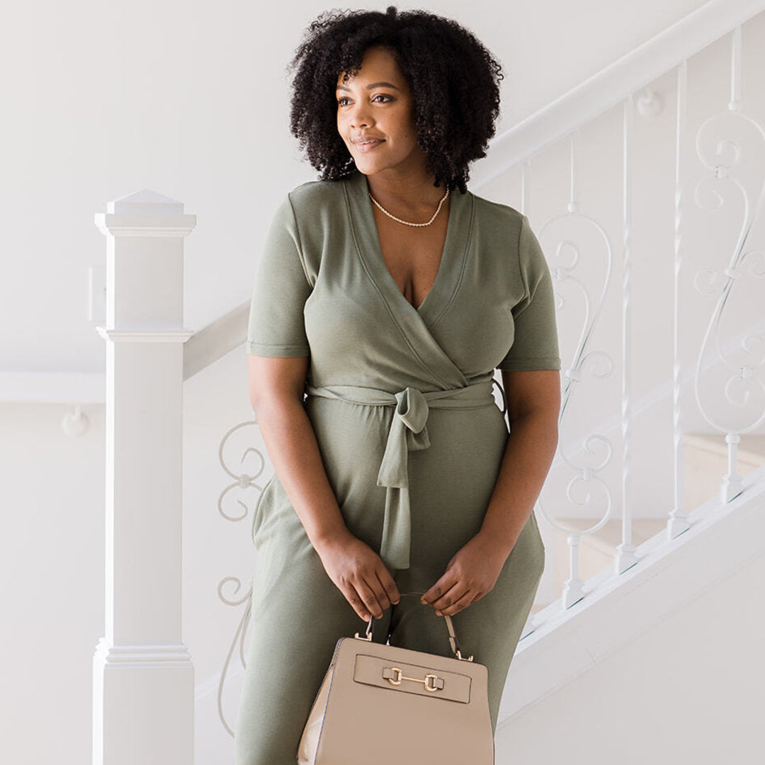 Model with her bag wearing the Around the Clock Nursing Jumpsuit in Olive.